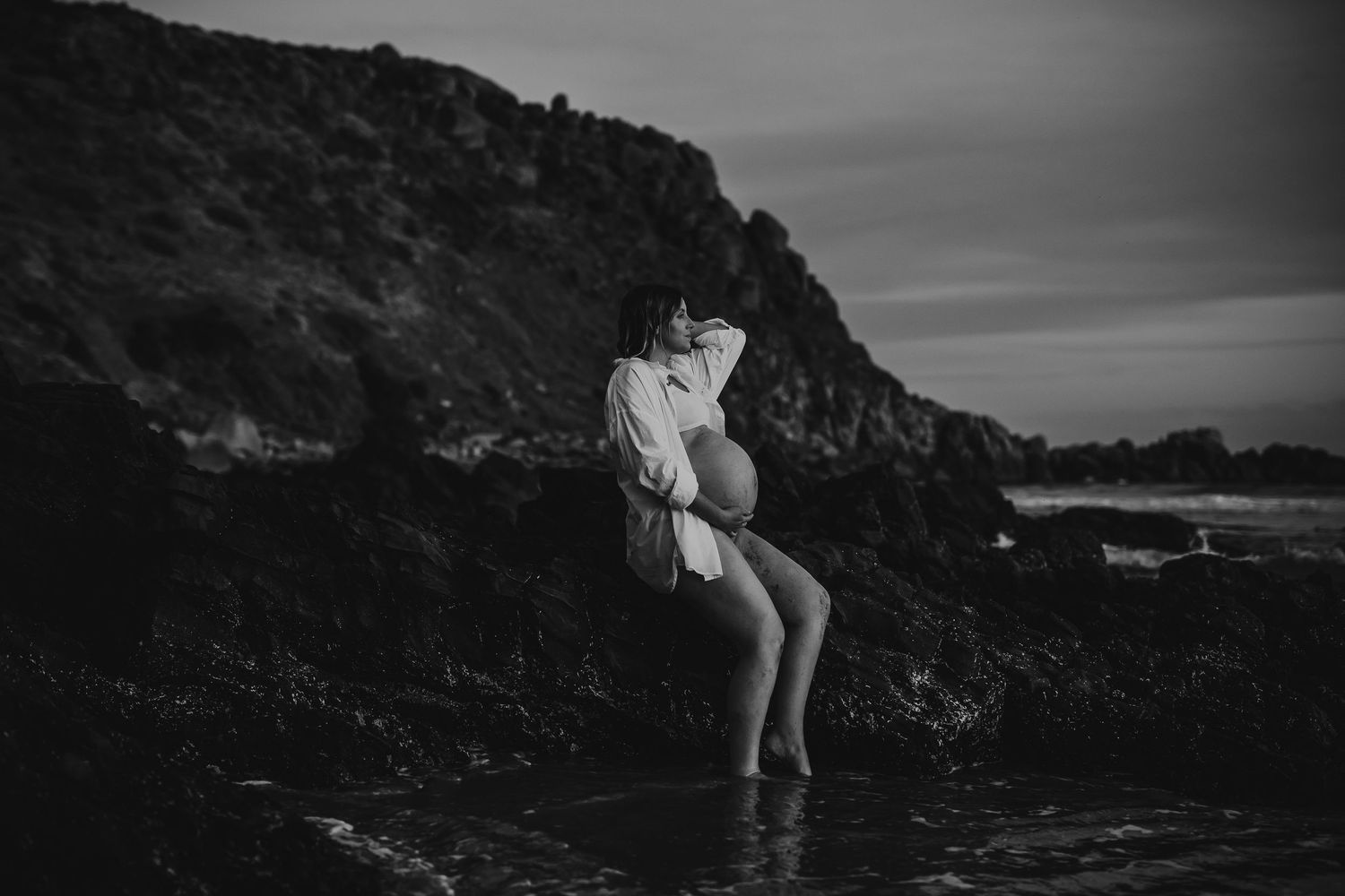 Outdoor maternity photo of pregnant mum sitting comfortably on rocks near the sea – South Australia