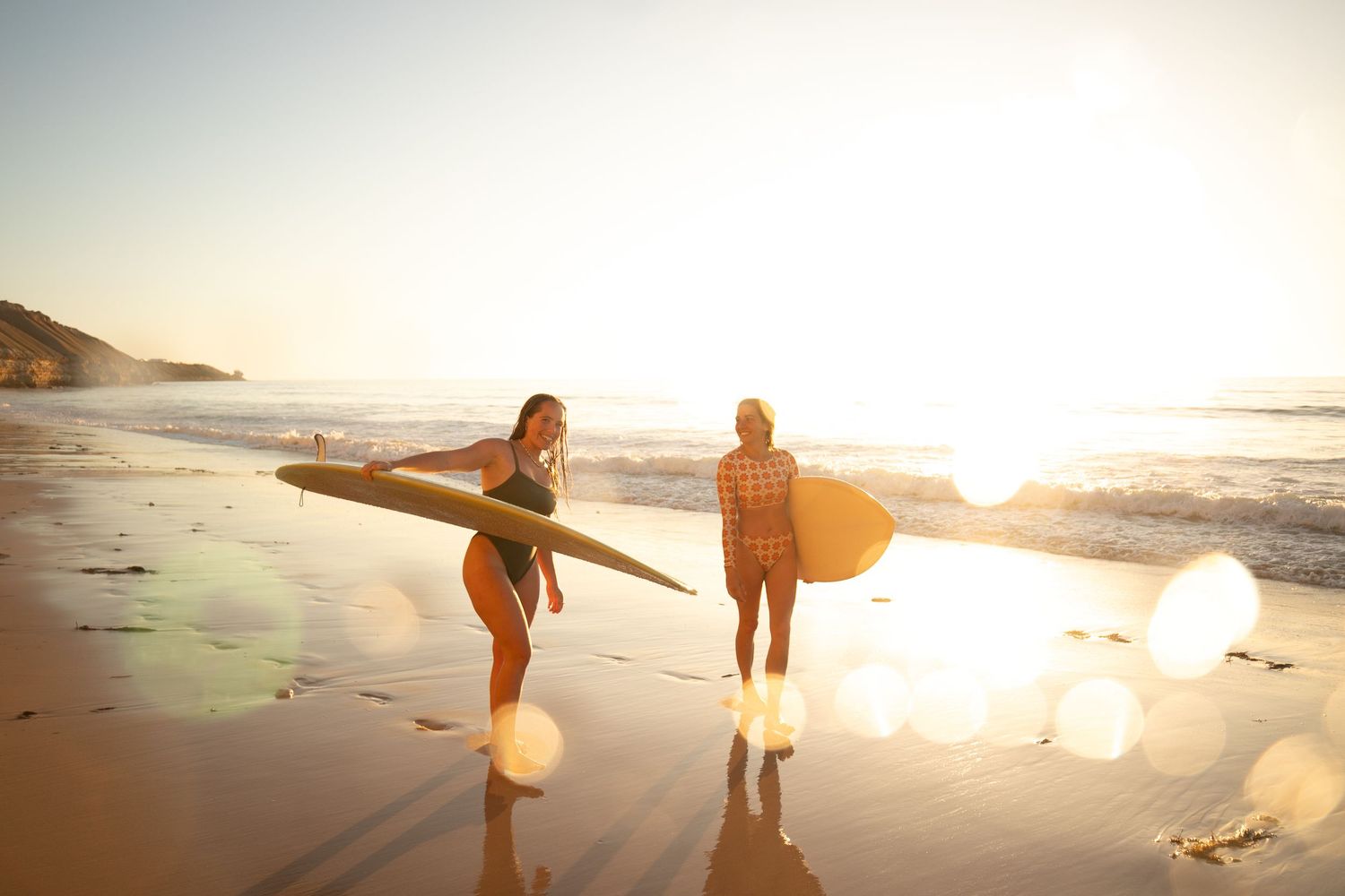 Two girls holding surfboards on Adelaide, South Australia beach at golden hour, warm sunlight and relaxed vibe