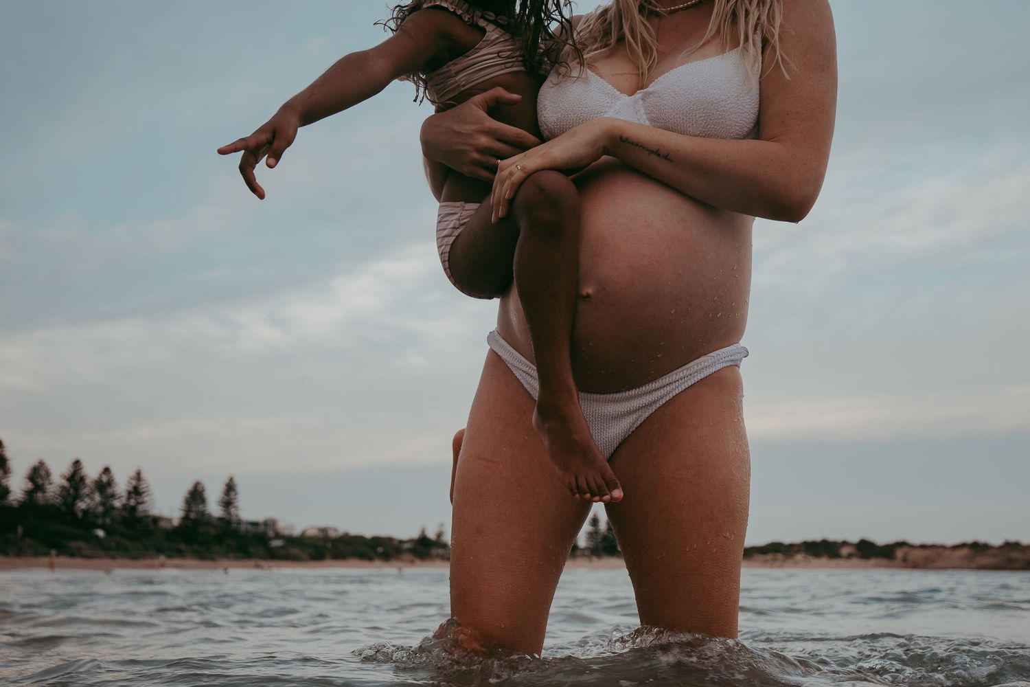 Minimalist beach maternity image showing belly and child being held – South Australia