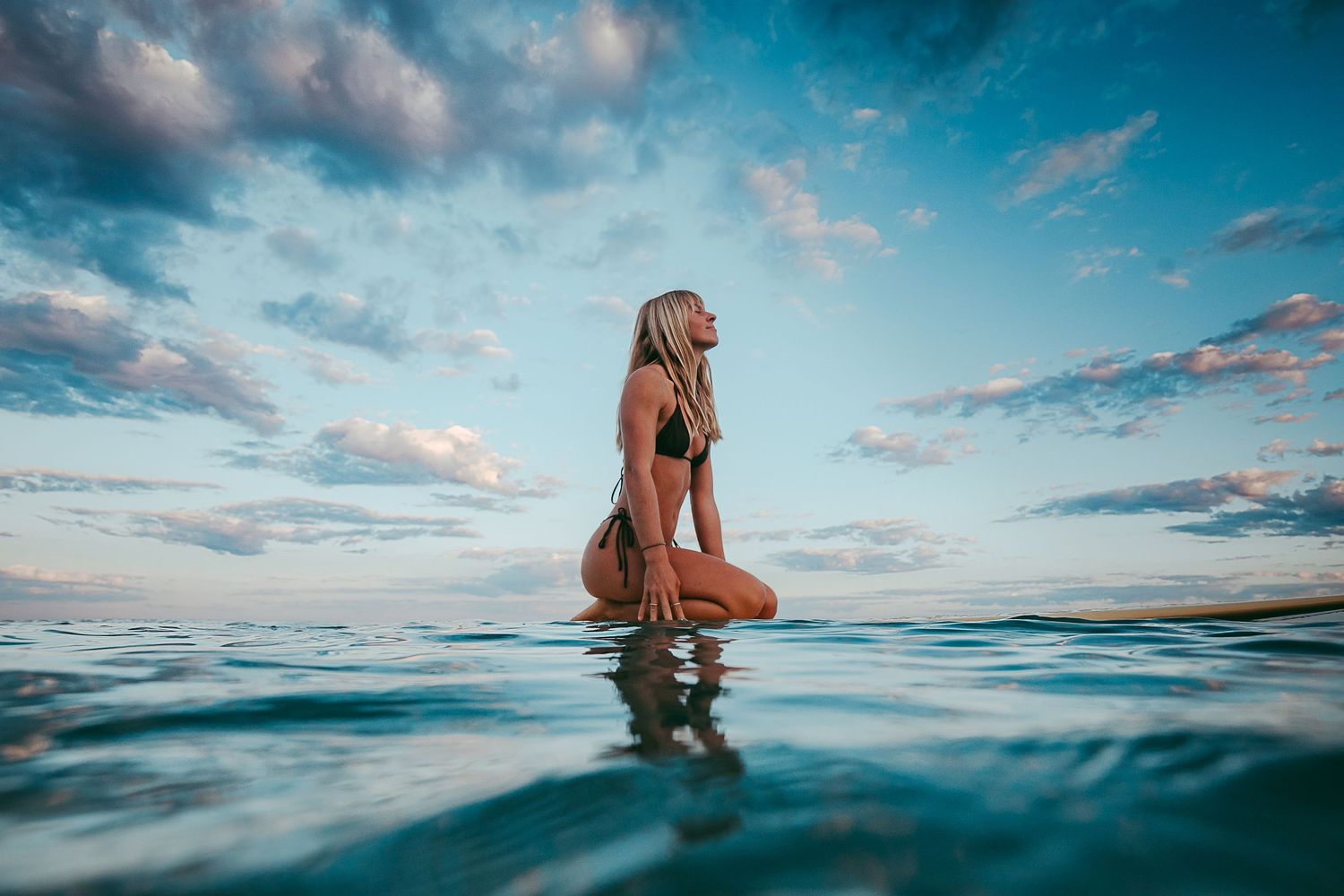 Lady sitting on a surfboard looking up at clouds.  Beautiful calm blue ocean.  Adelaide lifestyle and surf photographer.
