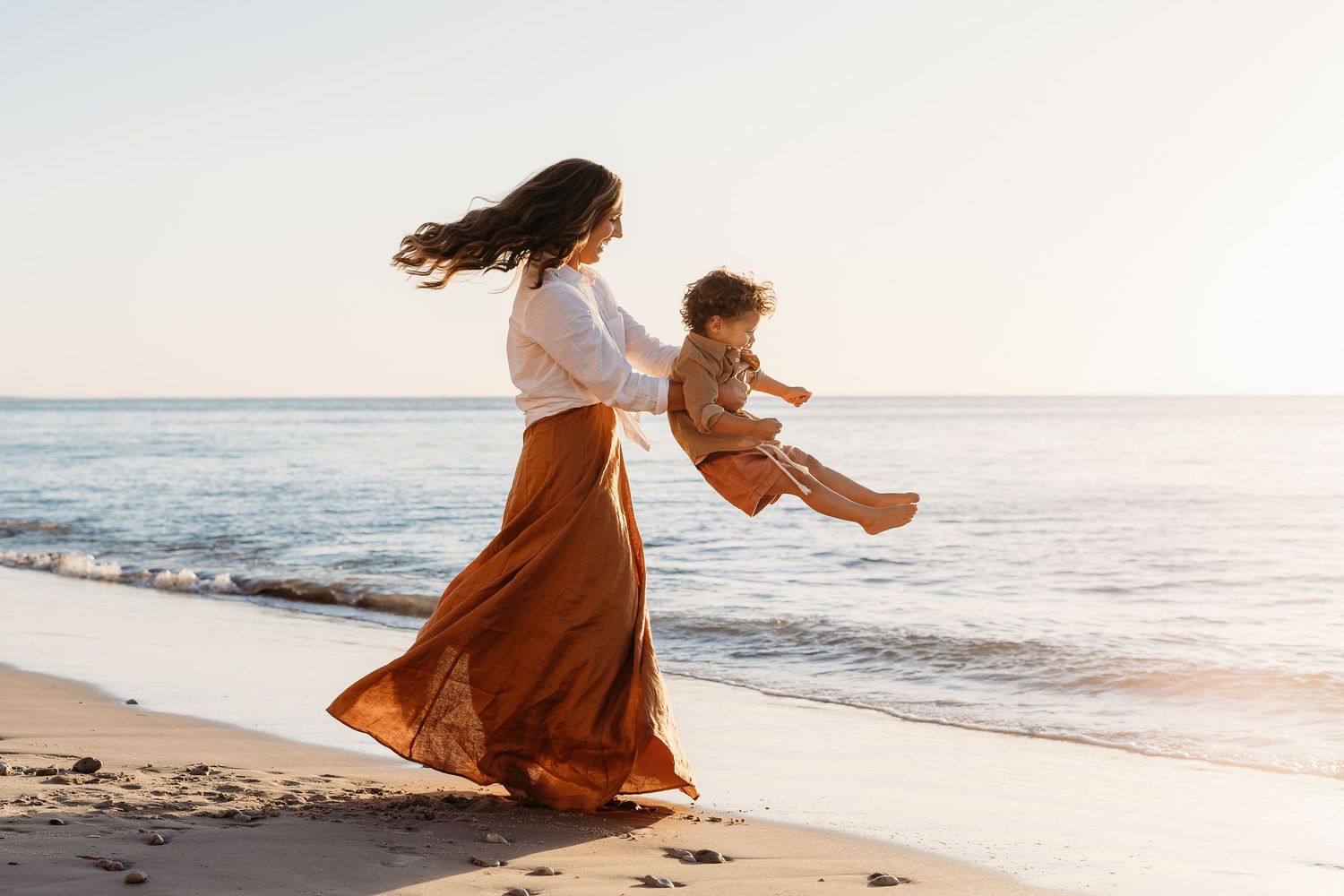 Mother spinning her child around joyfully on Adelaide beach, golden hour family moment