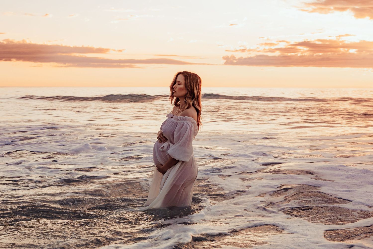 Maternity photo of expecting mum embracing baby bump in the sea – Raised by Water Photography