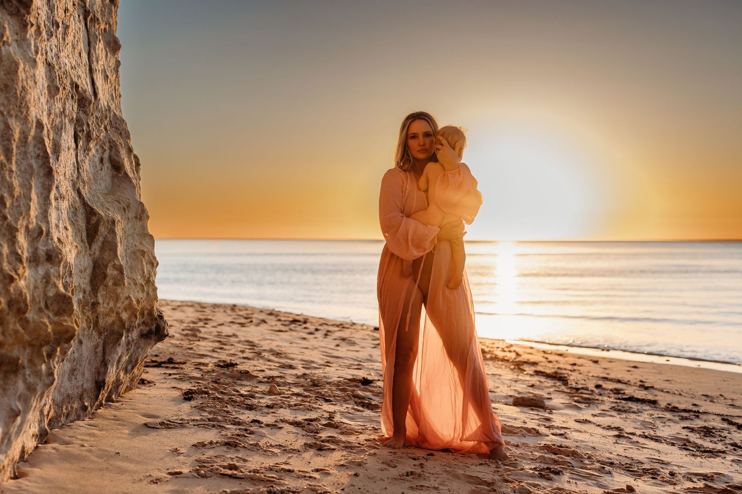 Mum cradling baby by the ocean during golden hour – South Australian beach photography