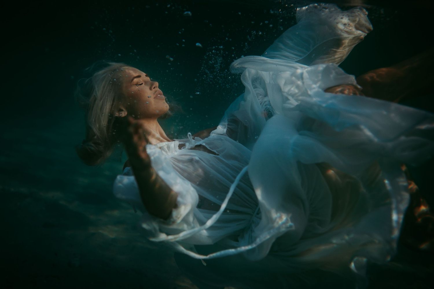 Artistic underwater maternity shoot with woman in white dress floating gracefully beneath the surface.  Adelaide, South Australia