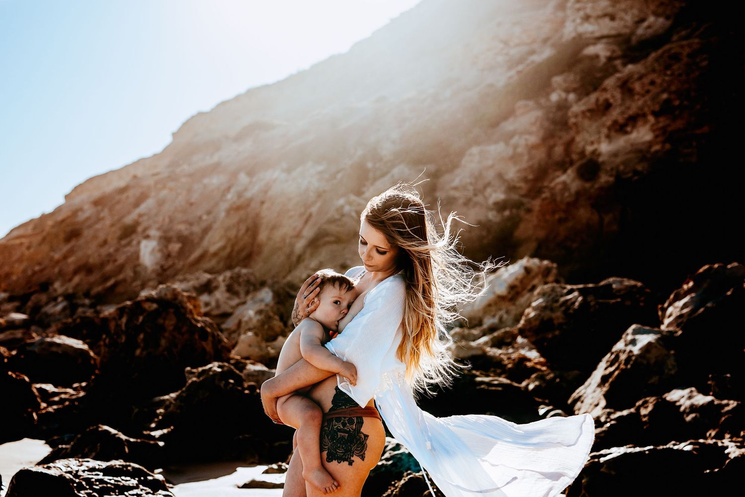 Natural light photo of mum breastfeeding child on beach by rocky cliffs – Adelaide family photography