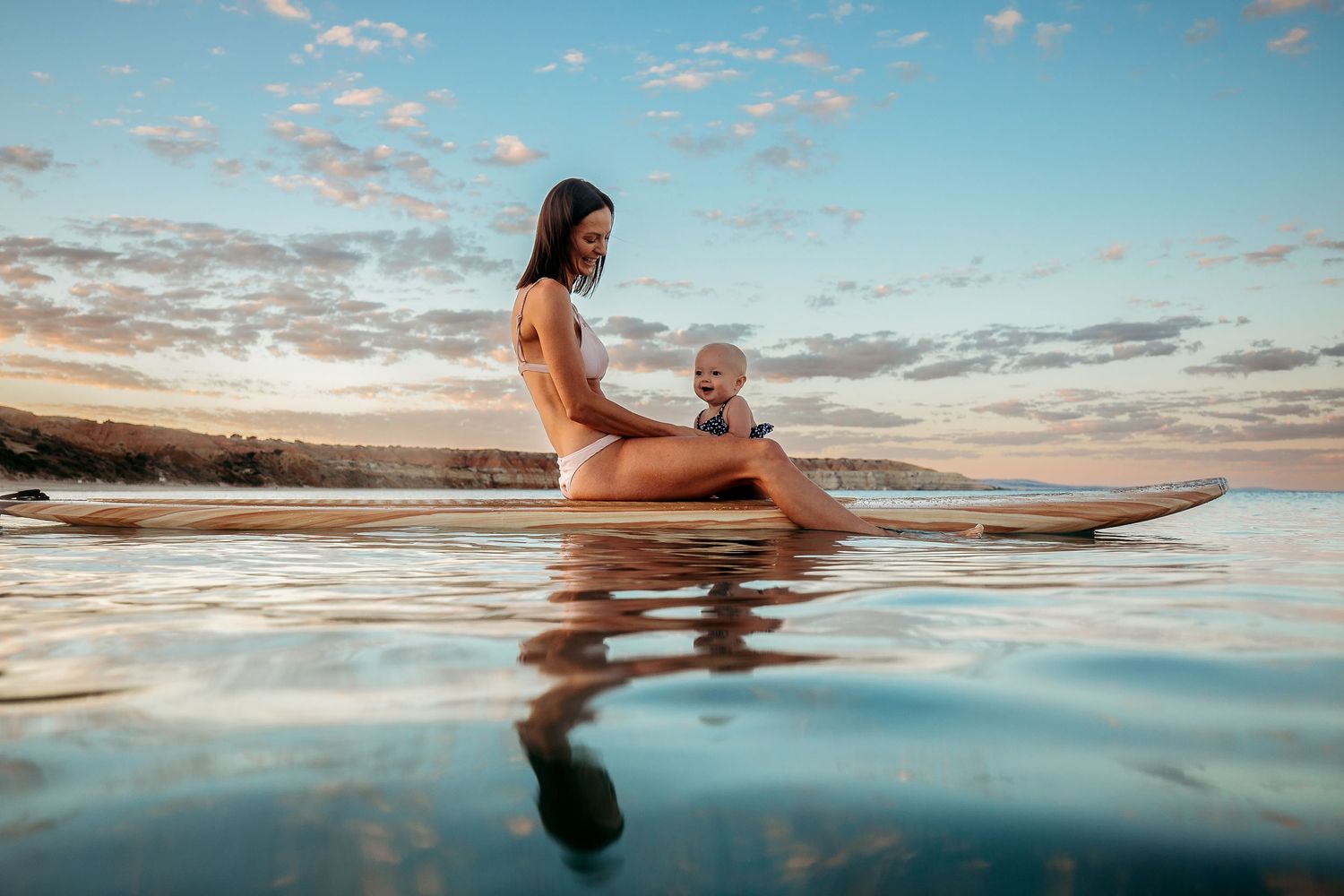 Mum sitting on a paddle board with her daughter in the clear calm ocean in Adelaide, South Australia