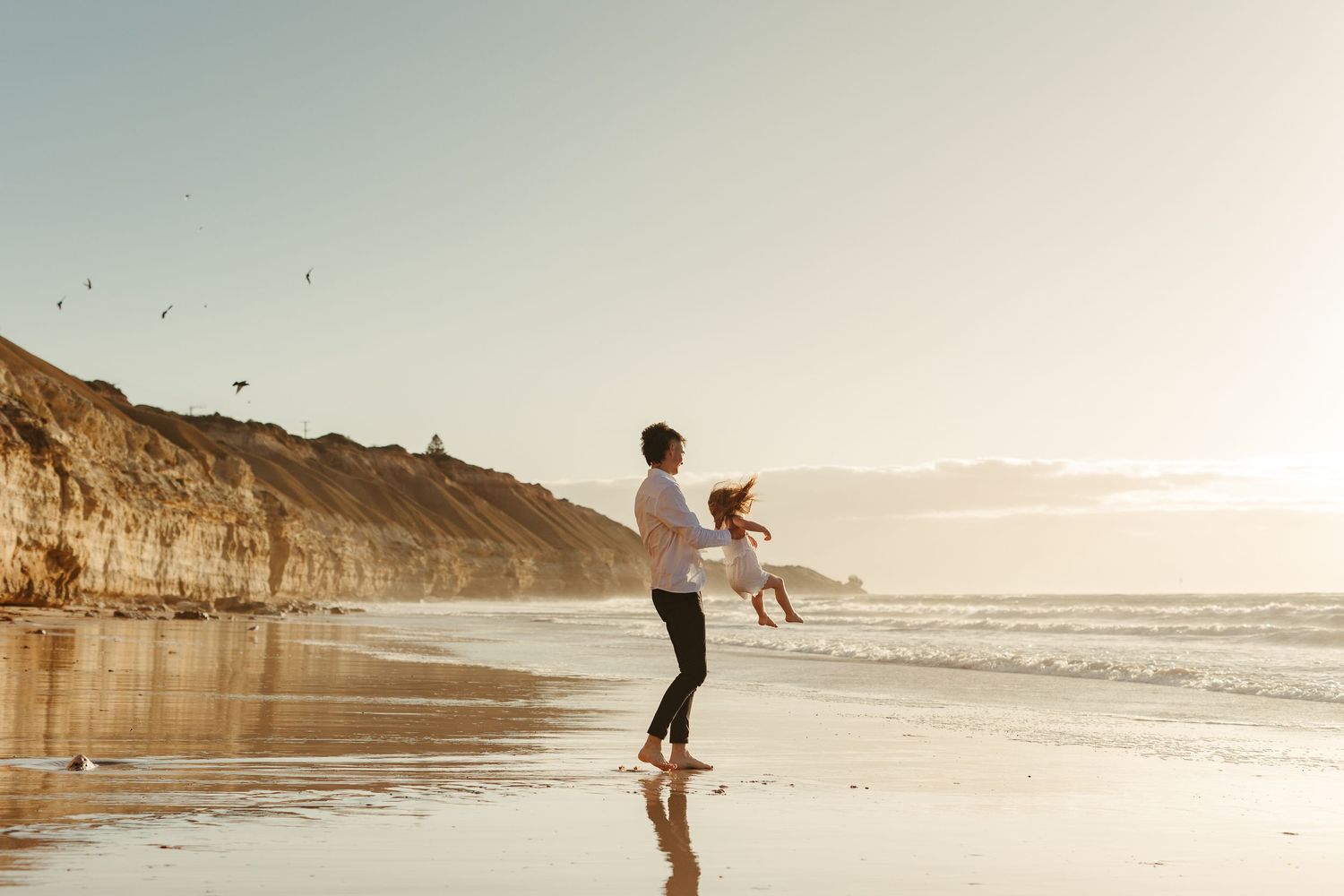 Dad spinning around his daughter on golden lit beach at sunset.  Adelaide family and lifestyle photographer - Raised by Water Photography