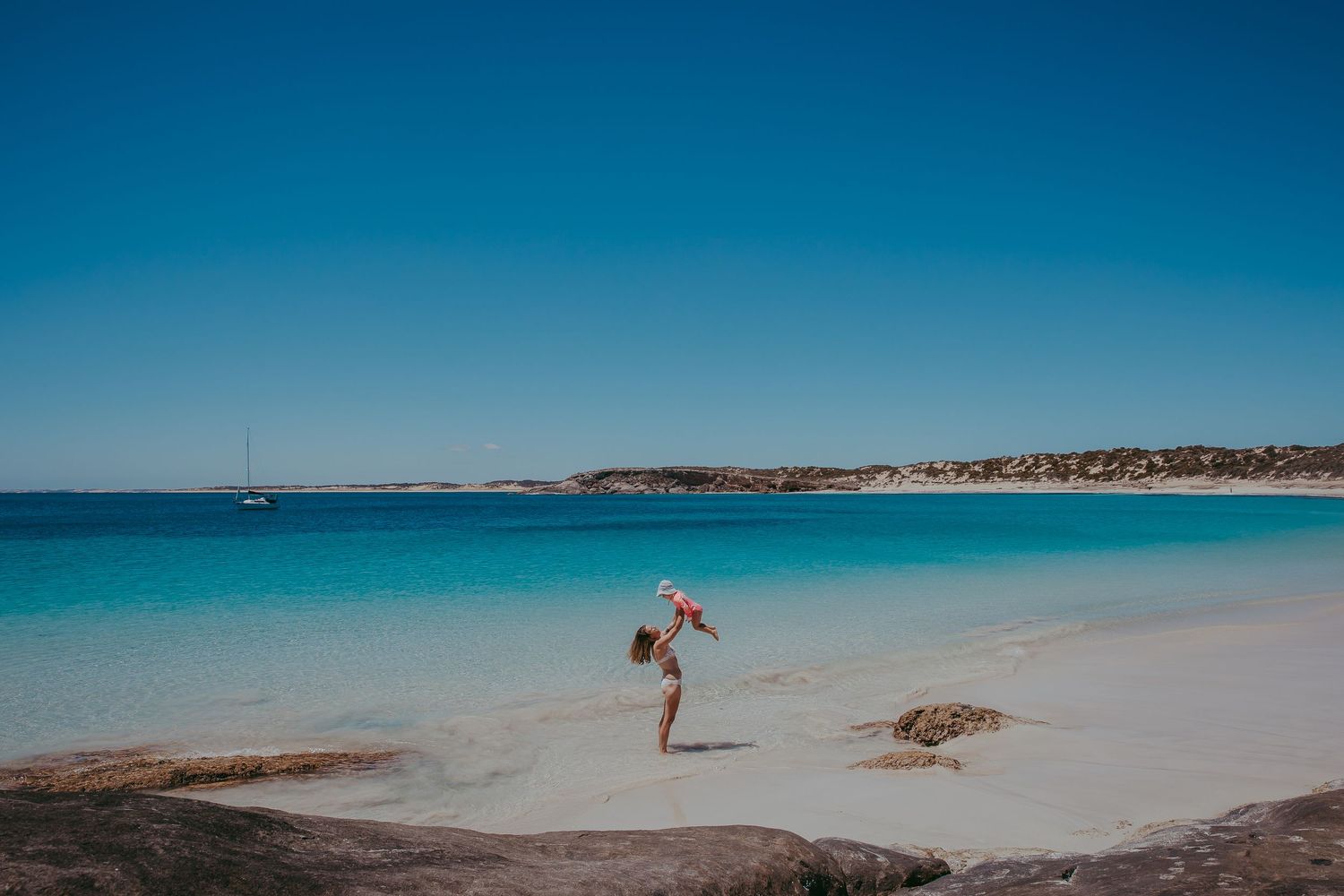 Playful photo of mother lifting child high on sandy shore – South Australia family photography