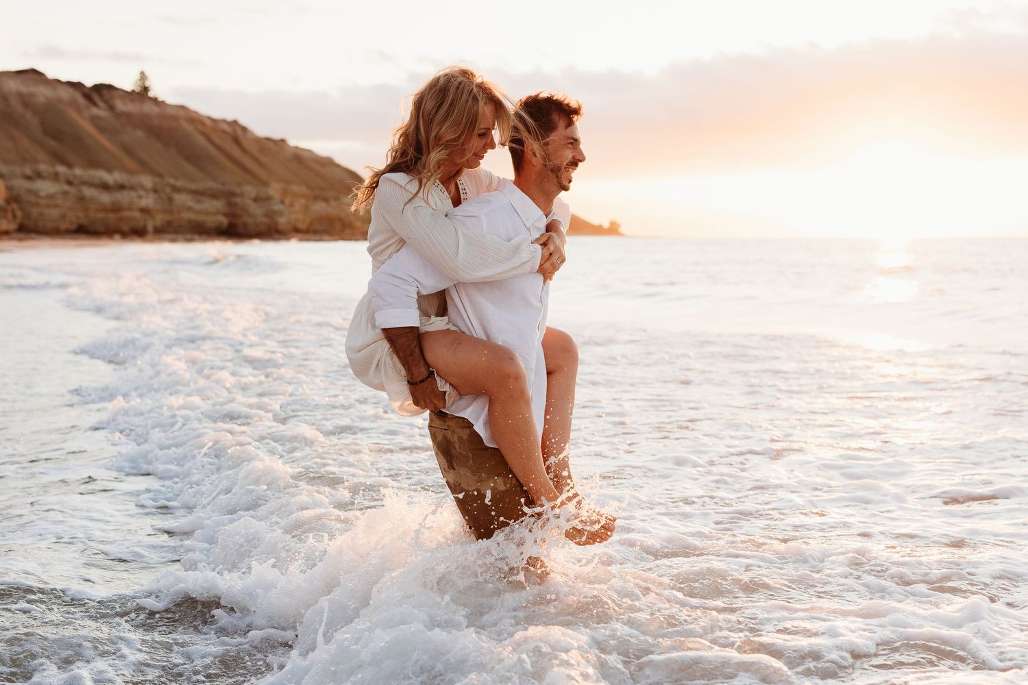 Man piggybacking his wife into the ocean at Adelaide beach – Raised by Water Photography Adelaide couple photographer