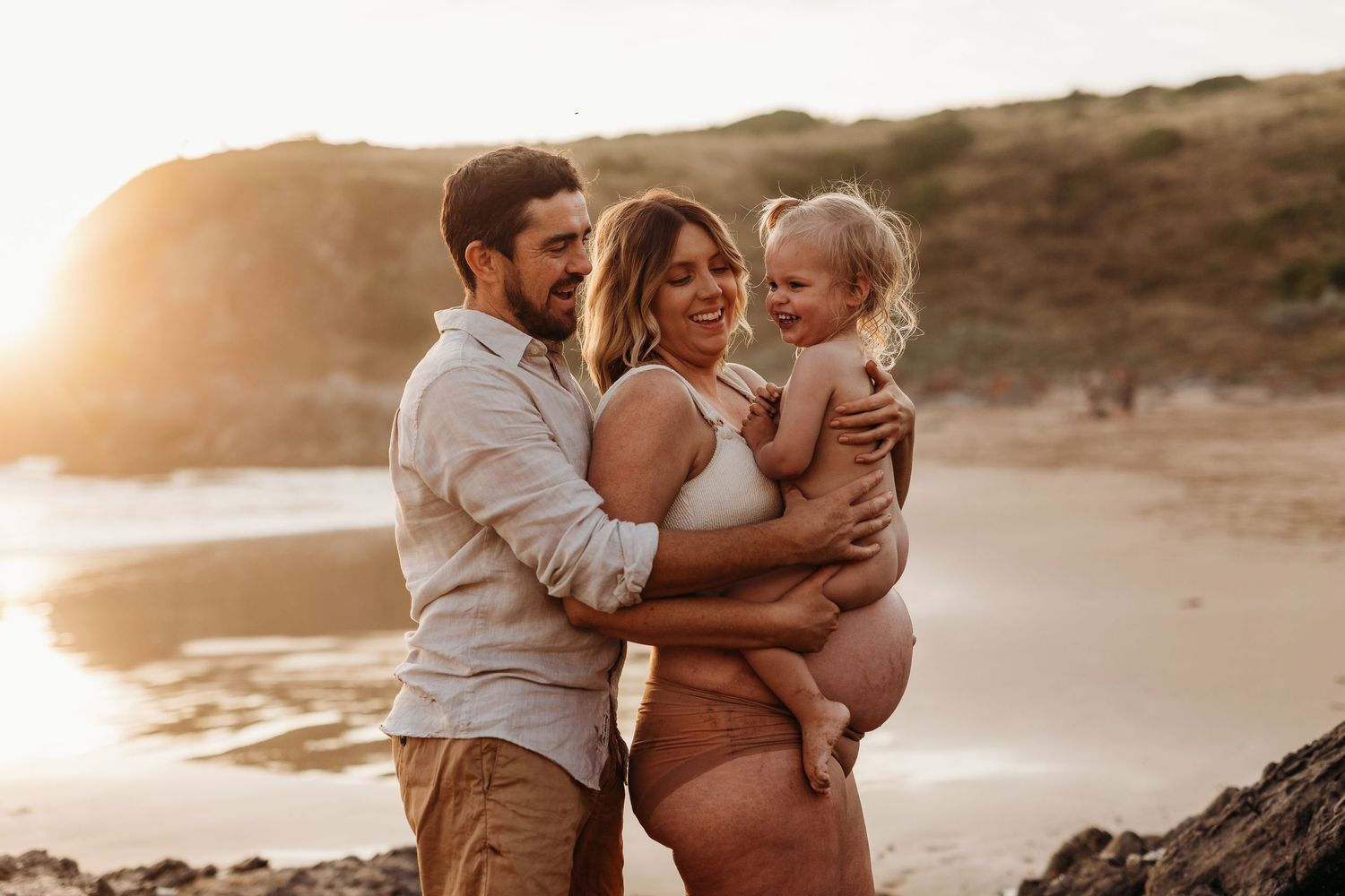 Tender family moment of expecting mother holding child as dad hugs her on the beach – South Australia lifestyle photography