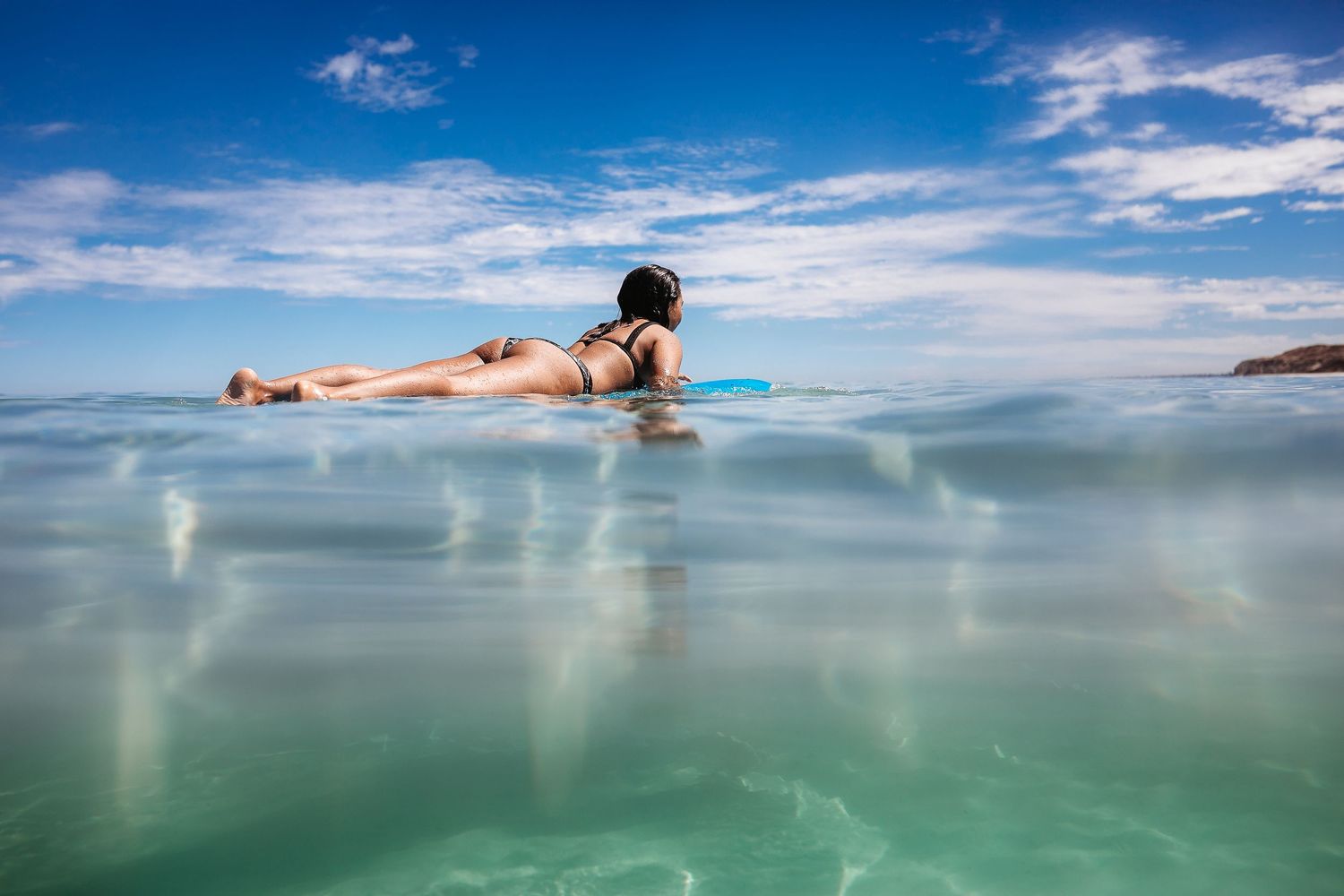 Woman floating on a surfboard in crystal clear ocean water near Adelaide, South Australia, peaceful and sunlit scene