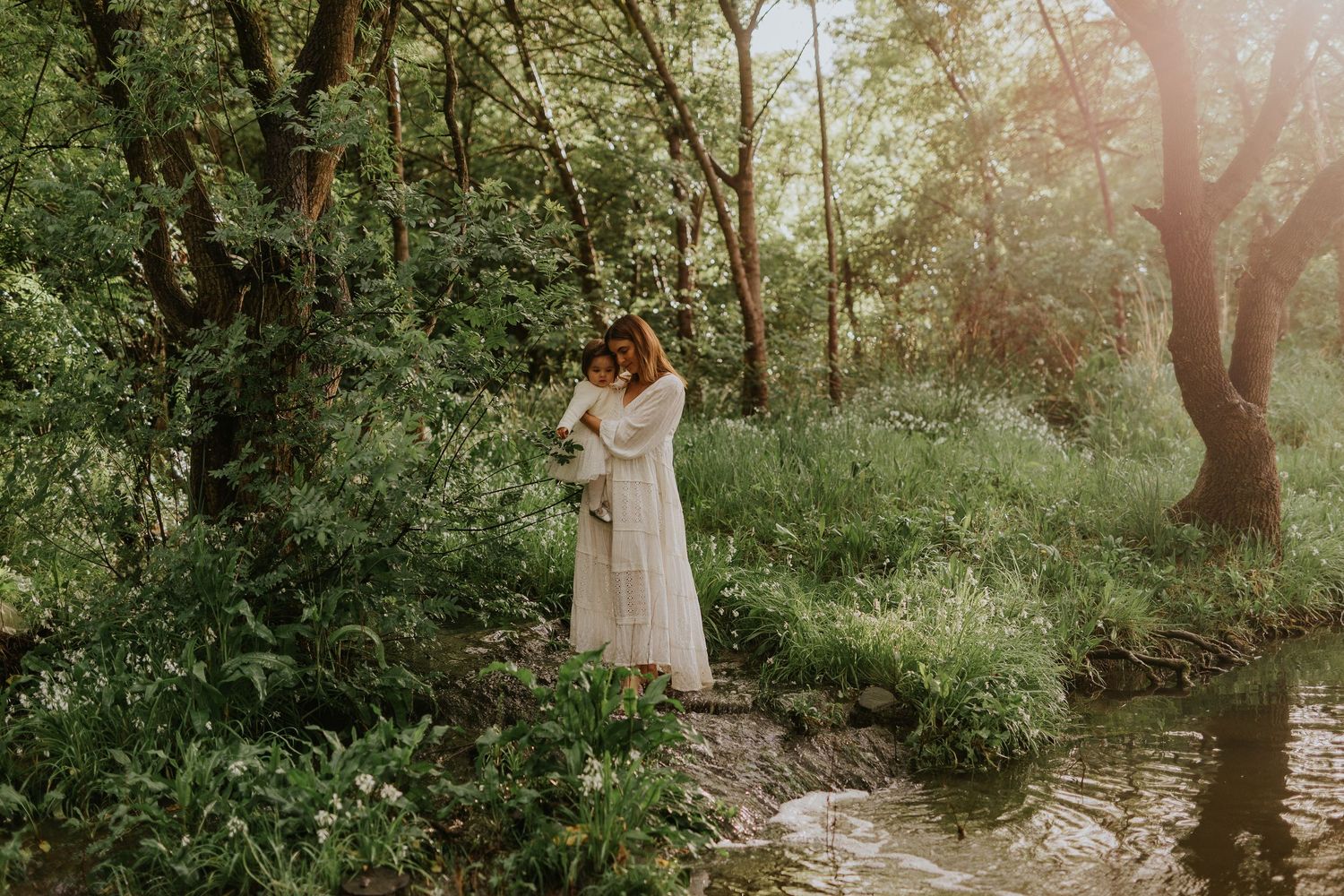Lady holding and embracing her child standing next to a creek with golden light.  Adelaide family lifestyle photographer
