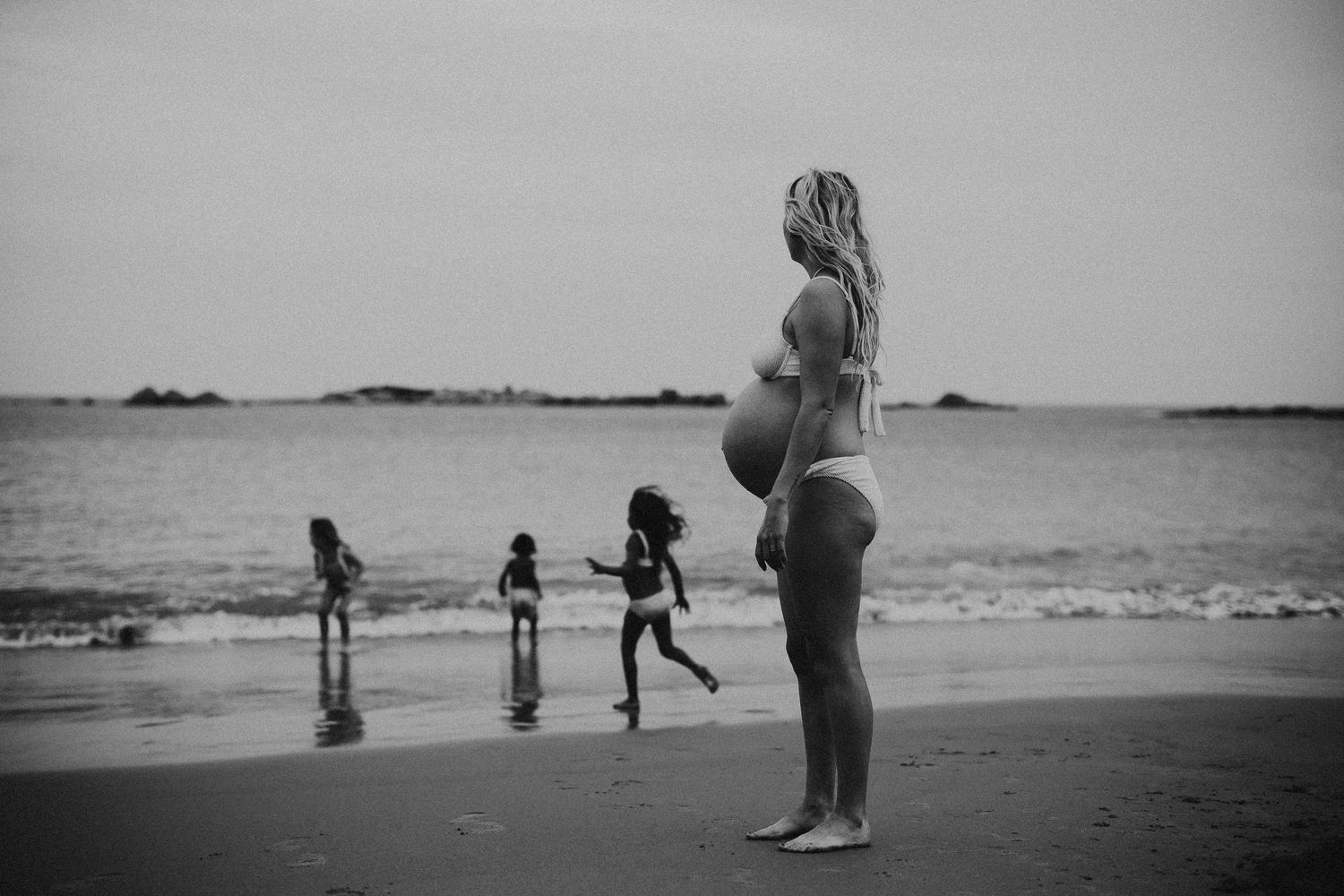 Pregnant mum standing on Adelaide beach with children running in the background – Raised by Water Photography
