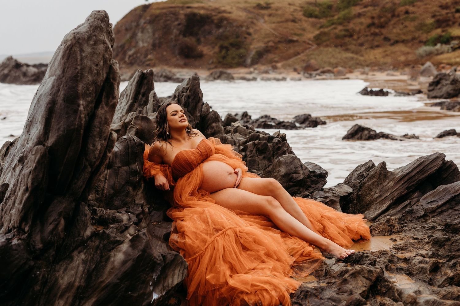 Lady leaning on a rock next to the ocean in a big gown - Adelaide maternity photographer South Australia