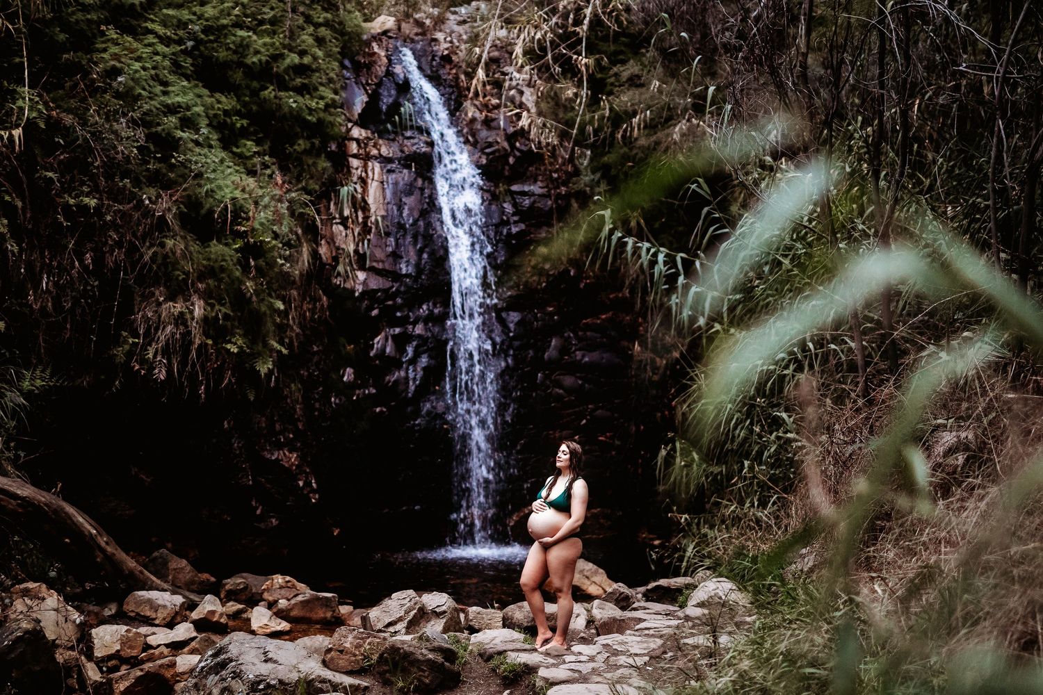 Serene image of pregnant woman standing by waterfall surrounded by lush nature – Raised by Water Photography
