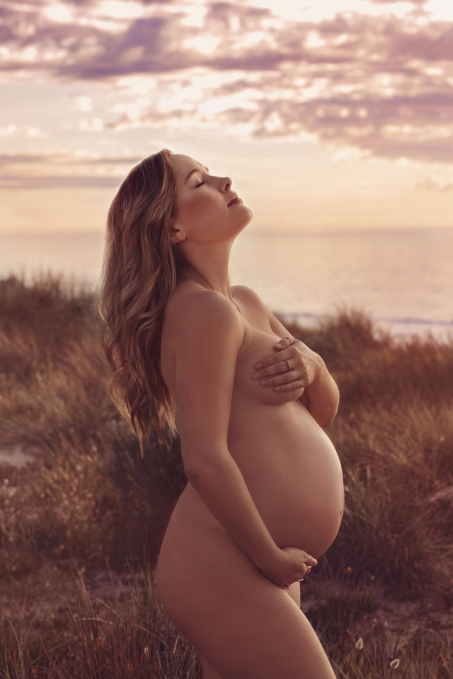 Raw maternity photography on South Australian beach — pregnant woman holding belly with ocean backdrop
