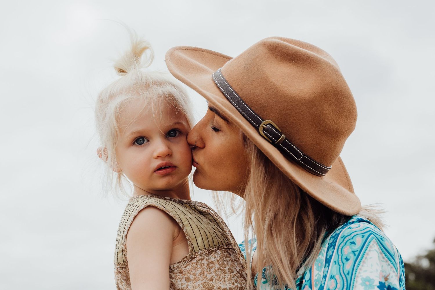 Mum kissing her daughter on the check while looking at camera.  Adelaide motherhood photographer
