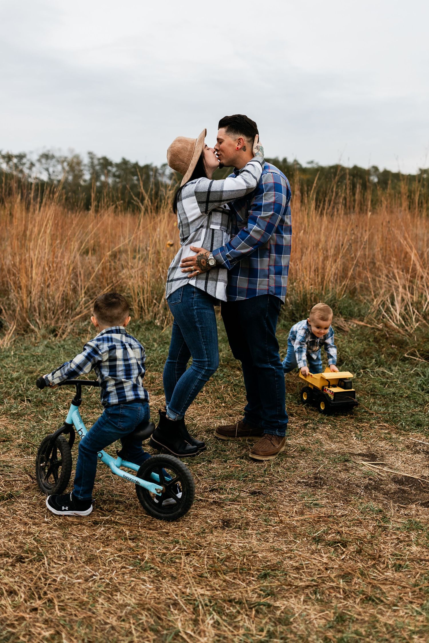 Family shares tender moment in field while children play with bike and toys. bold and emotional family photography sessions in des moines, i
