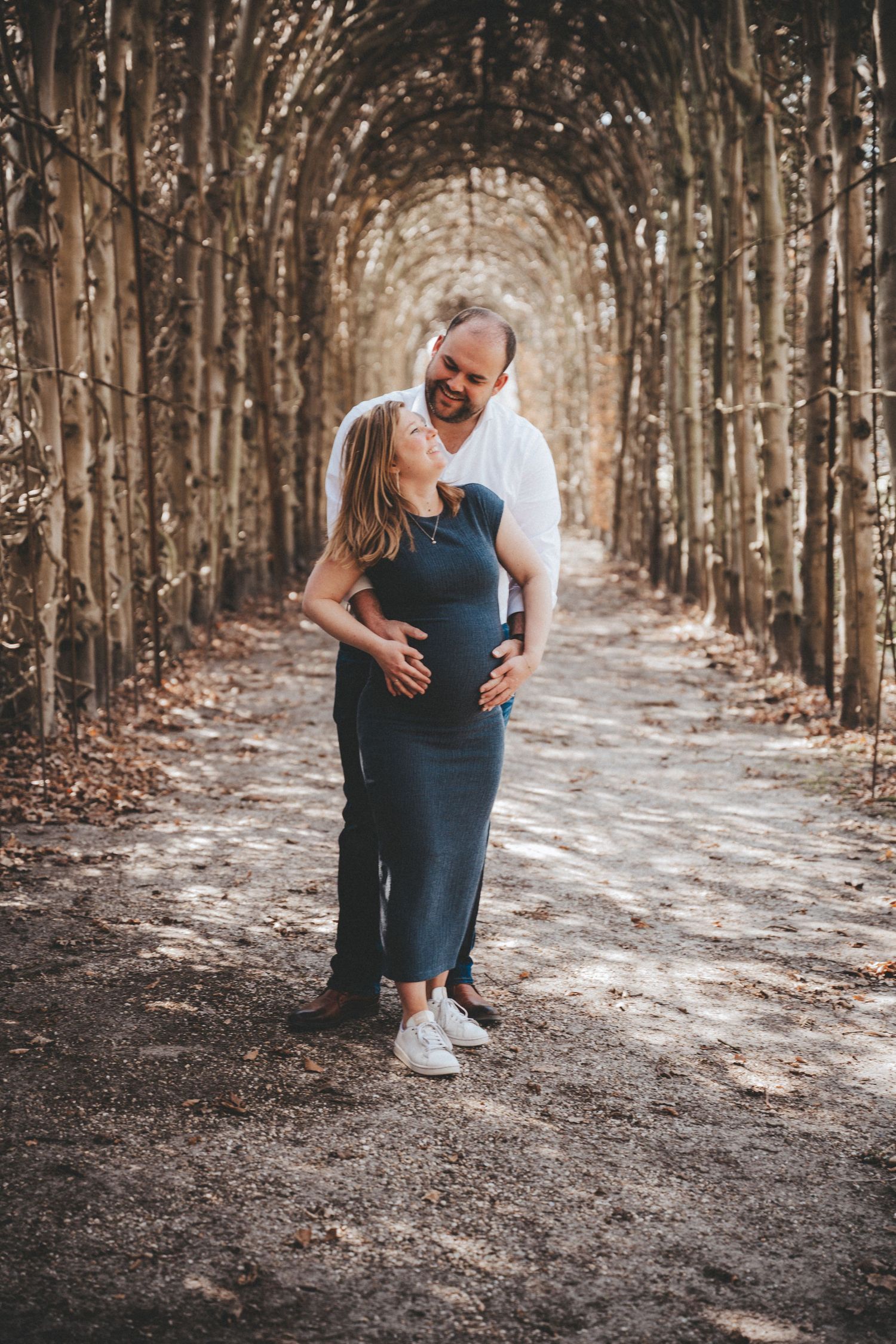 Romantic maternity photos taken in a tree-lined path with natural outdoor lighting.