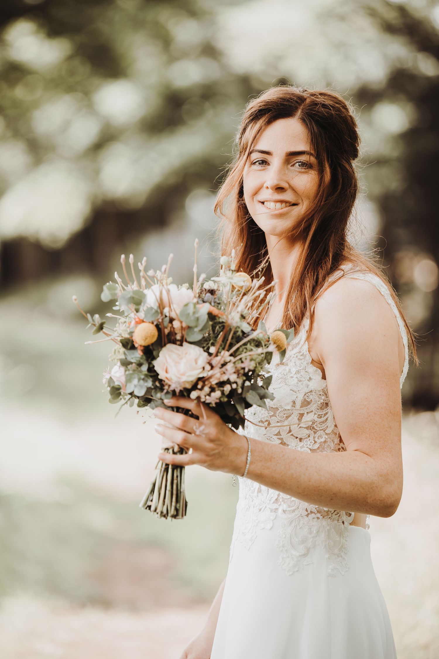 Beautiful bouquet of wildflowers and dried elements in soft neutral tones against a dreamy outdoor backdrop.