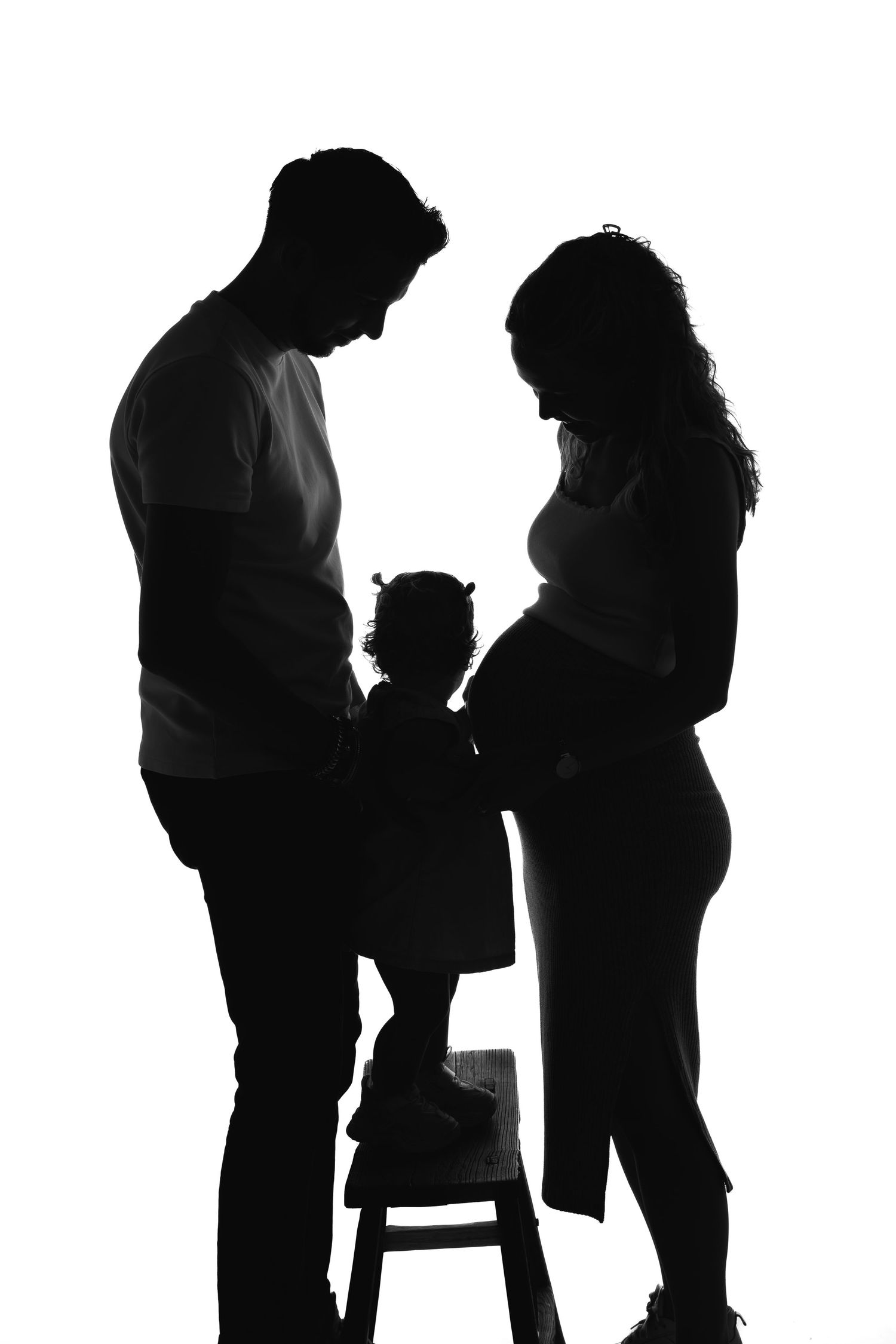 Silhouette of family with child standing on stool between parents.