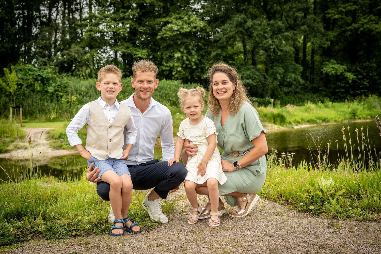 Family relaxes together on grassy path during outdoor photo session.