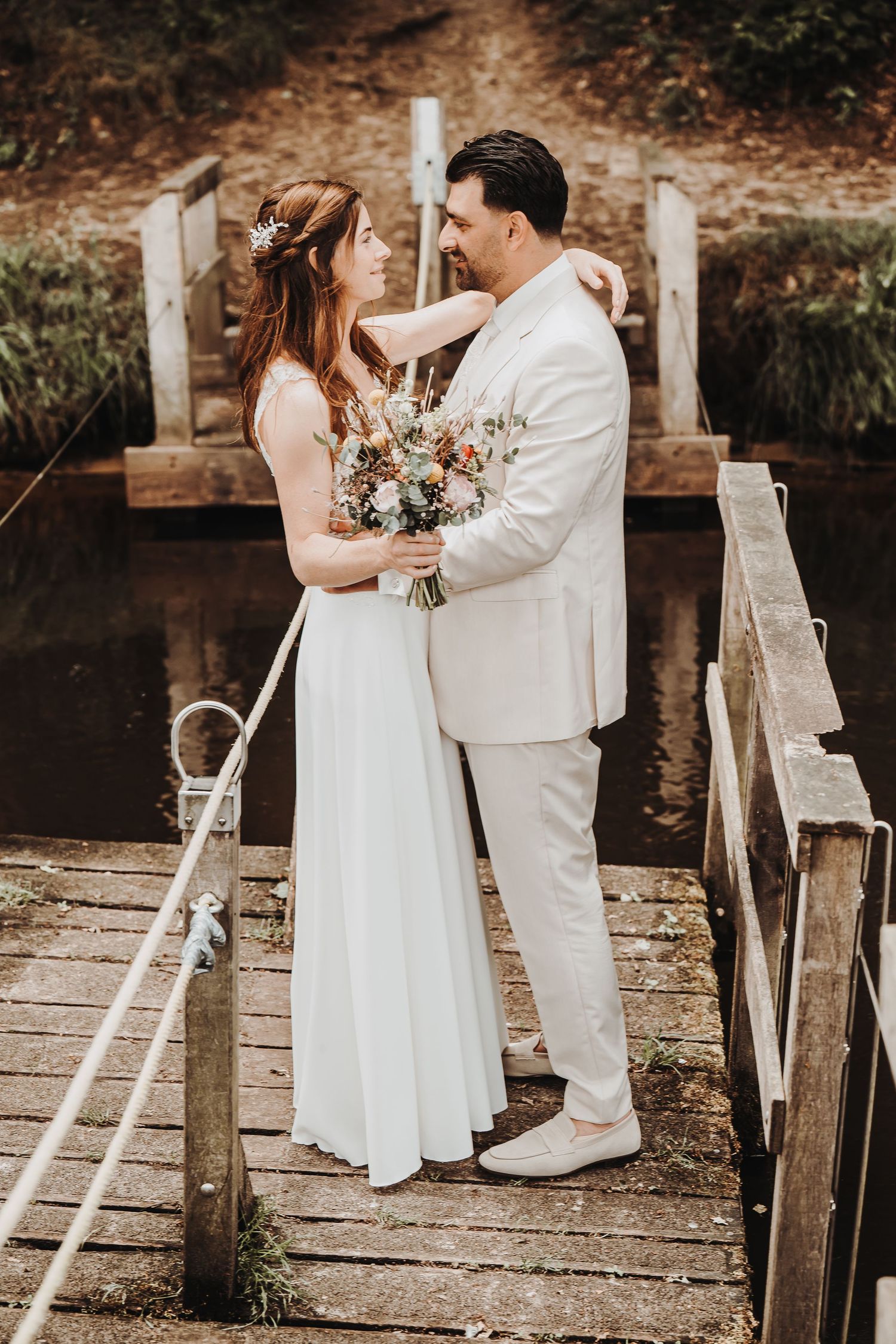 Romantic couple in white attire embracing on rustic wooden steps.
