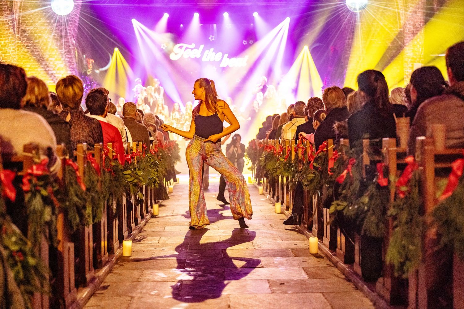 Concert venue with purple and yellow lighting effects illuminating an audience-lined walkway.
