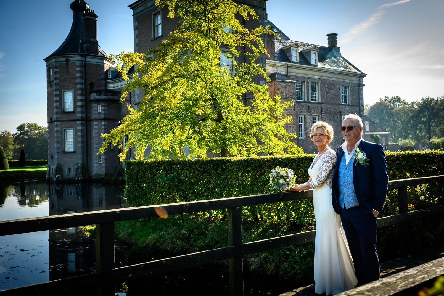 Couple posing outside a grand stone mansion with bright green foliage.