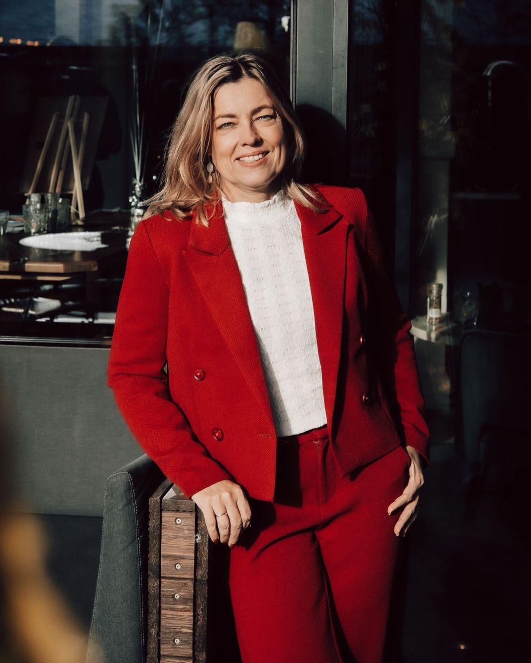 Woman in bright red blazer poses confidently against urban backdrop.
