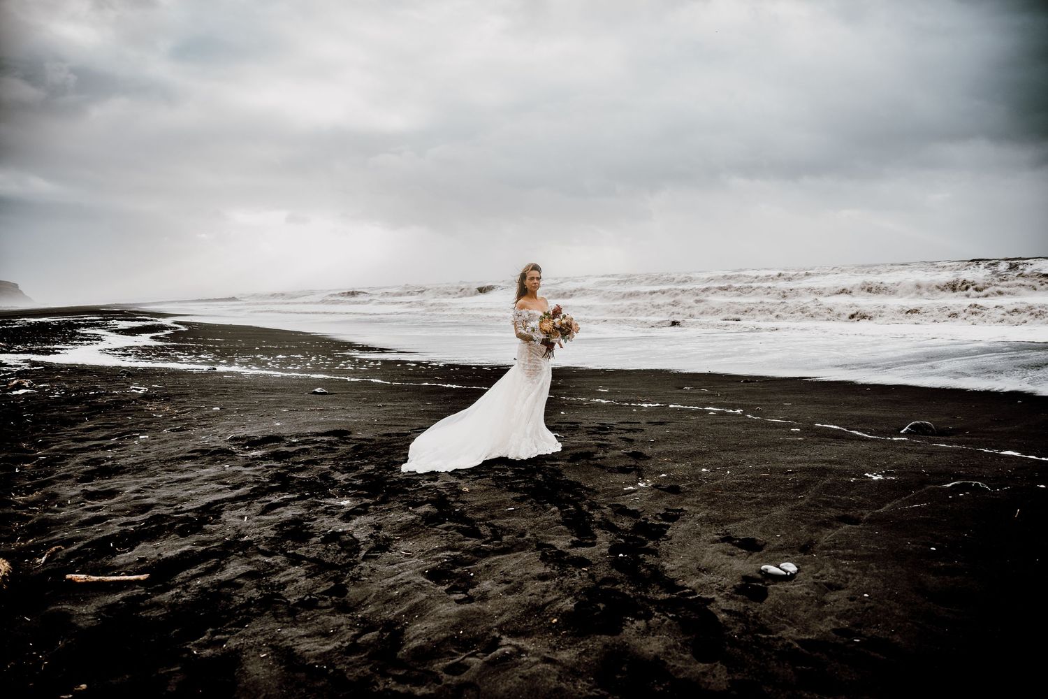 A dramatic black and white beach wedding photo shoot with crashing waves and dark volcanic sand.