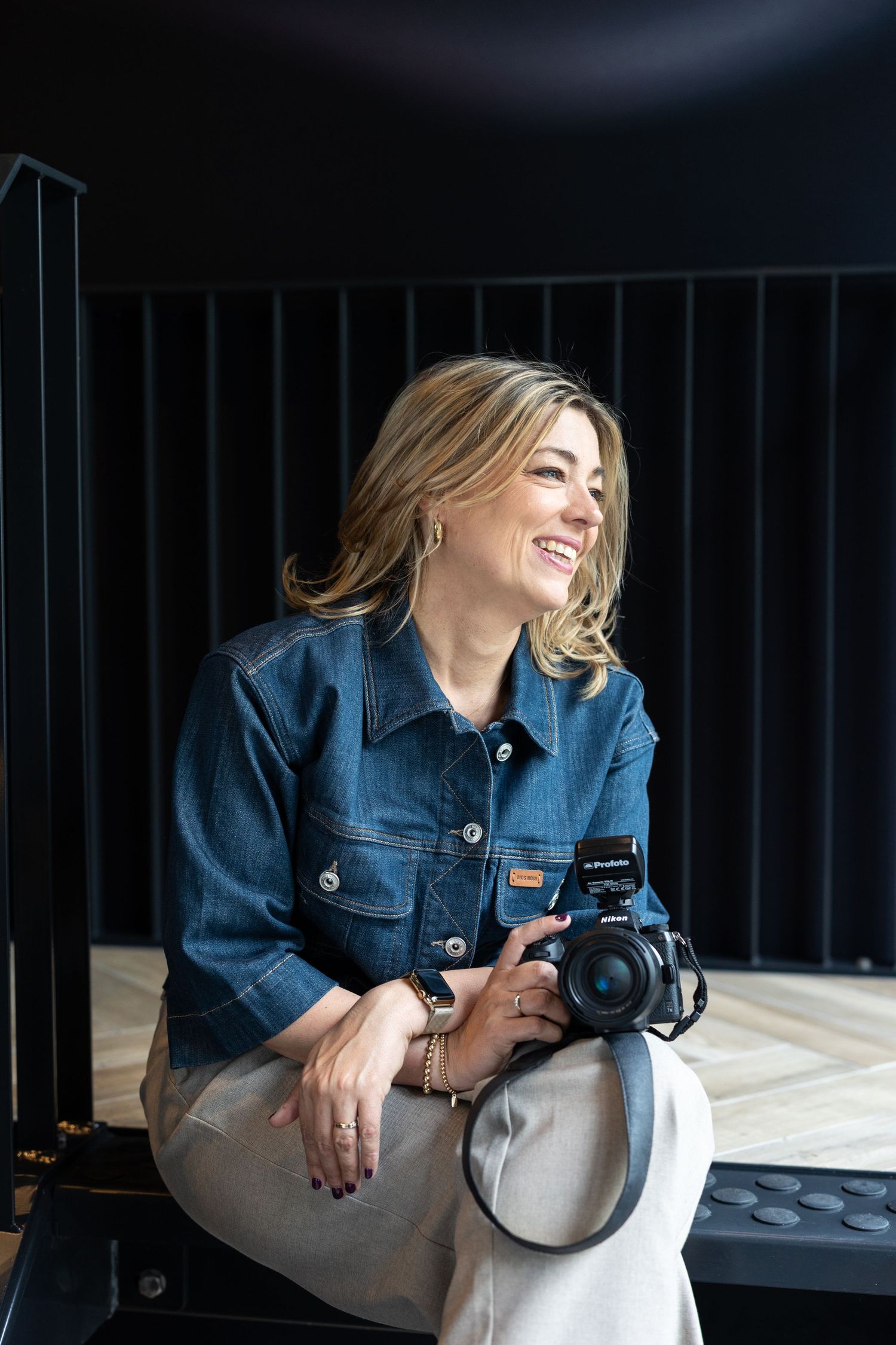 Professional photographer in denim jacket working with camera equipment in studio setting.