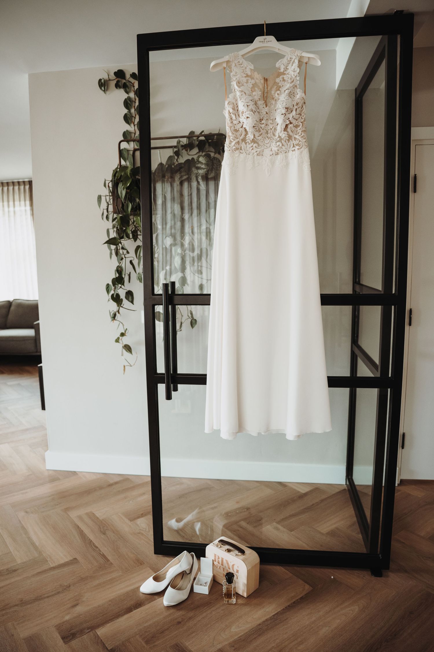 White lace wedding dress hanging on display with shoes beneath in a modern room with herringbone floors.