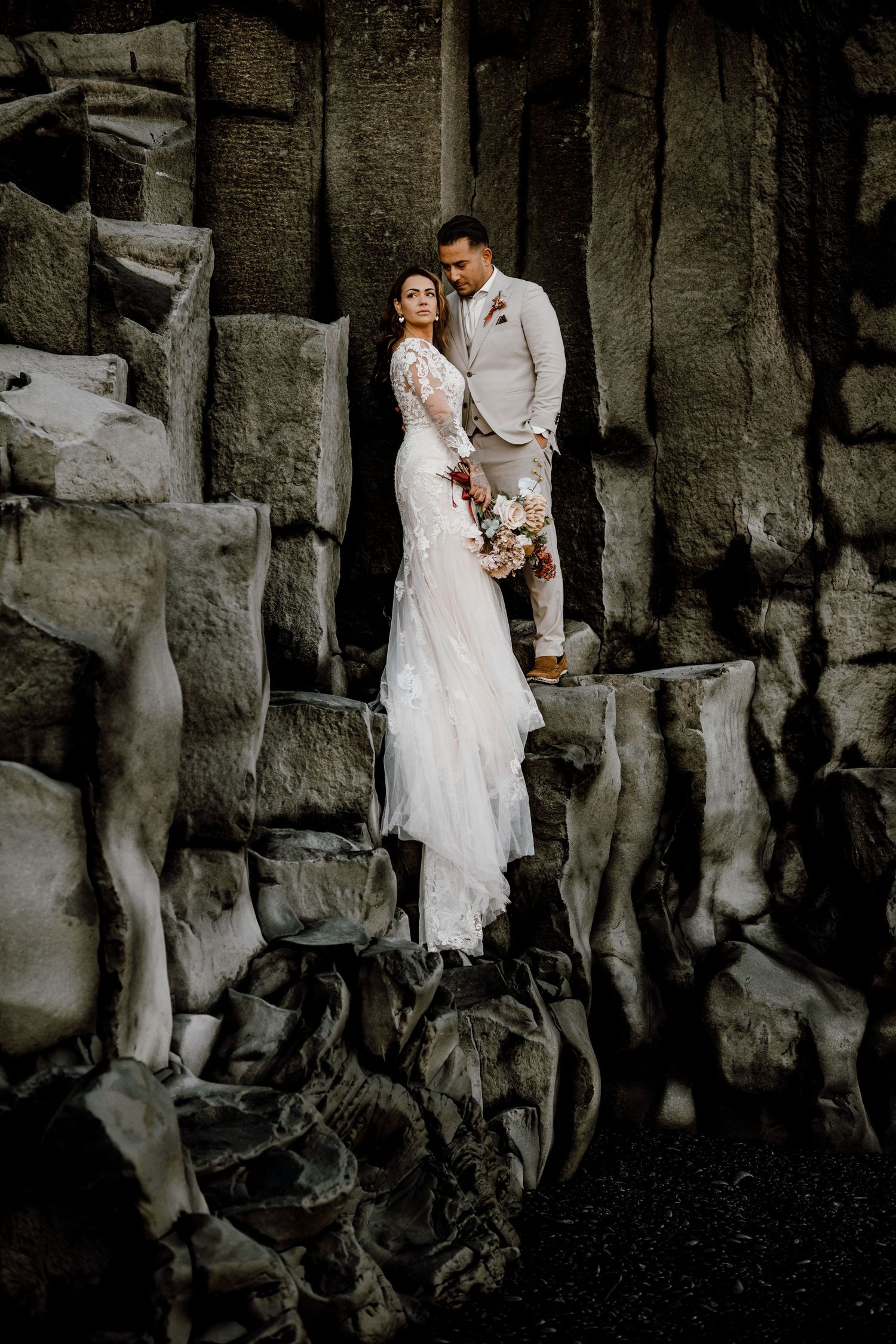 A couple shares an intimate moment against a textured rock wall backdrop during their wedding photoshoot.