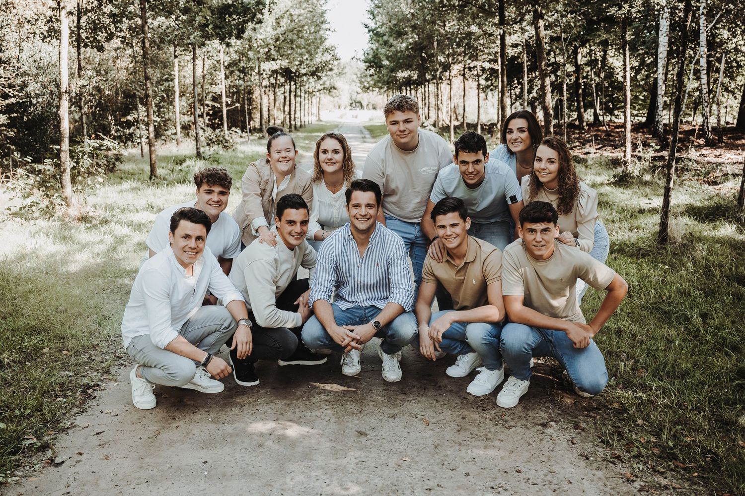 A casual group photo session outdoors with people sitting and standing on grass in coordinated outfits.