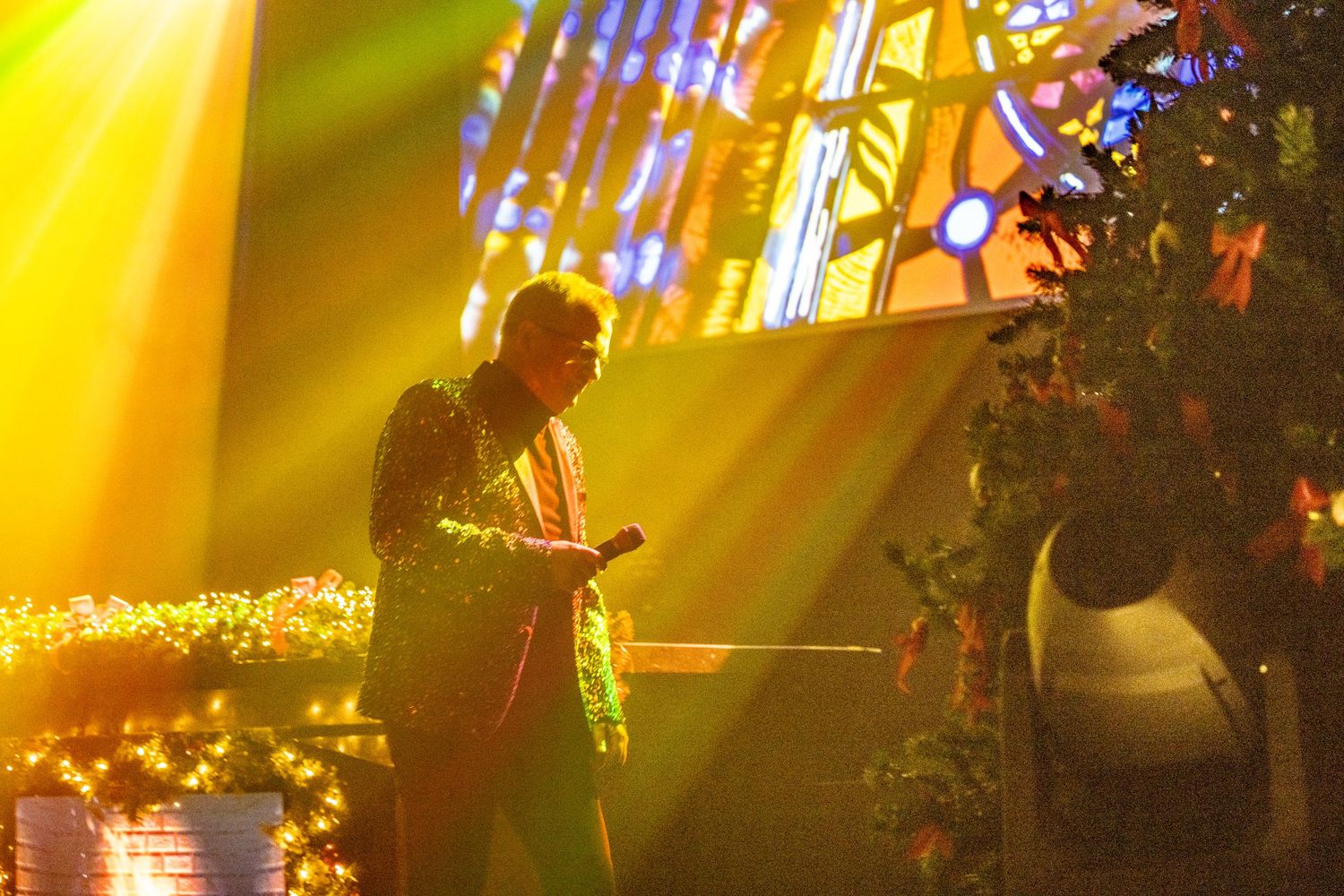 Dramatic concert stage with vibrant yellow lighting and colorful stained glass window backdrop.