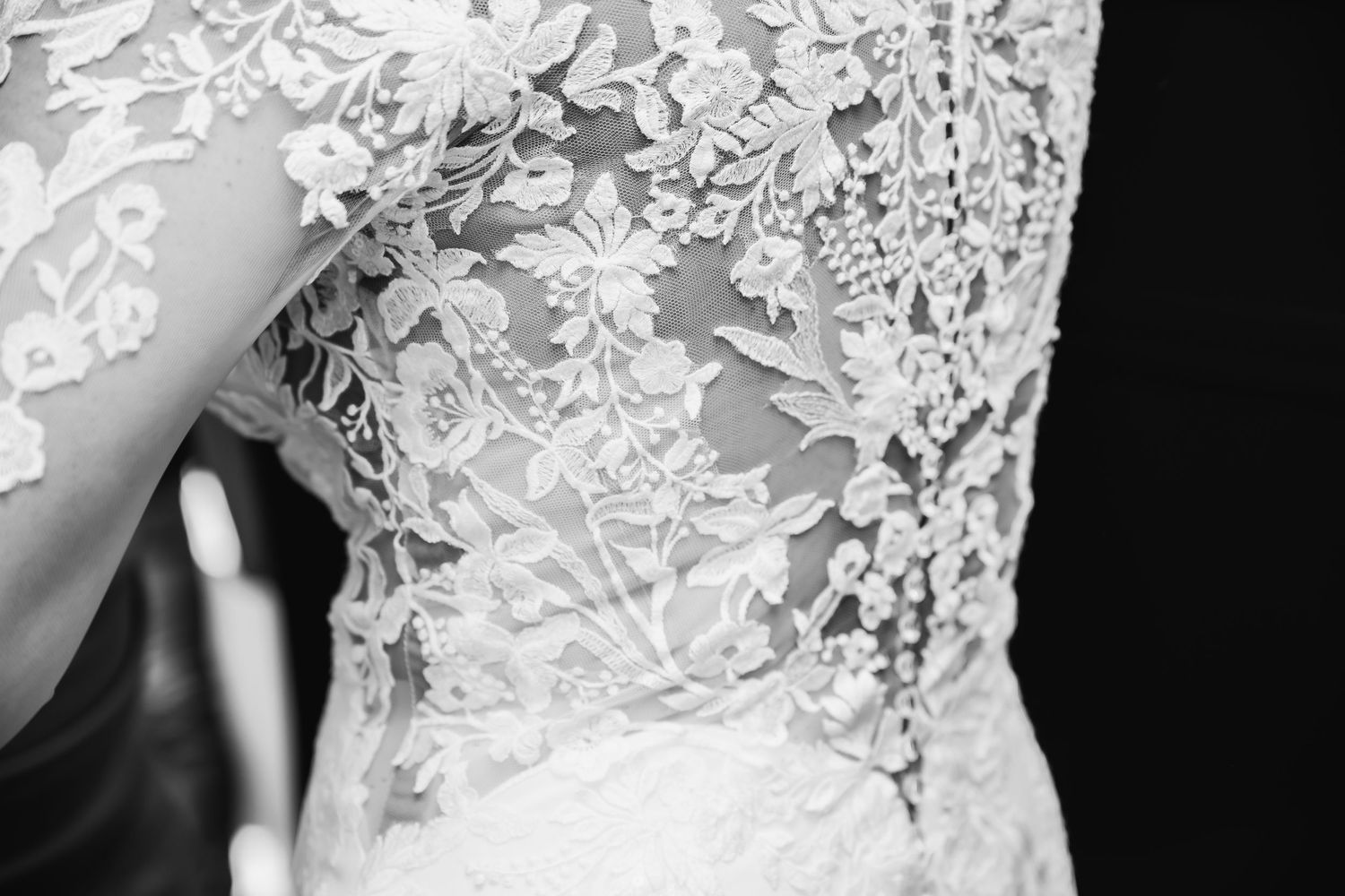 Close-up details of an elegant white lace wedding dress with intricate floral patterns.