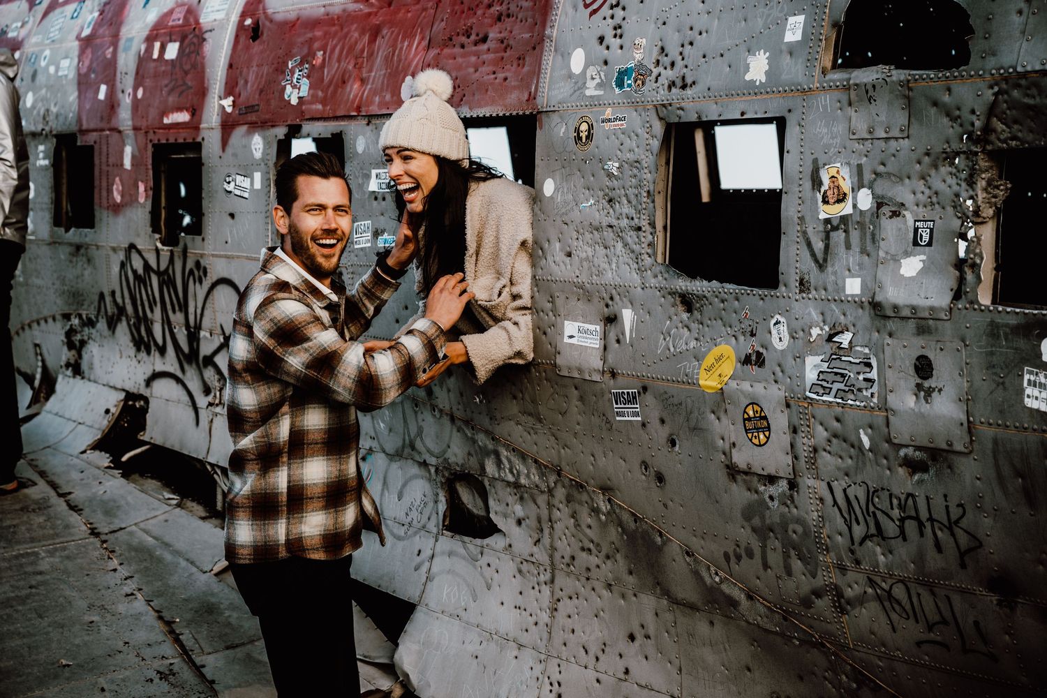 A person in a plaid shirt stands against a graffiti-covered concrete wall in an urban alleyway.
