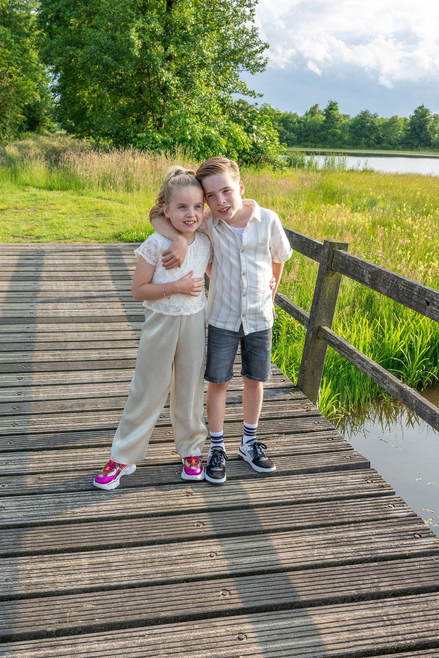 Children playing together on wooden boardwalk surrounded by lush summer greenery.