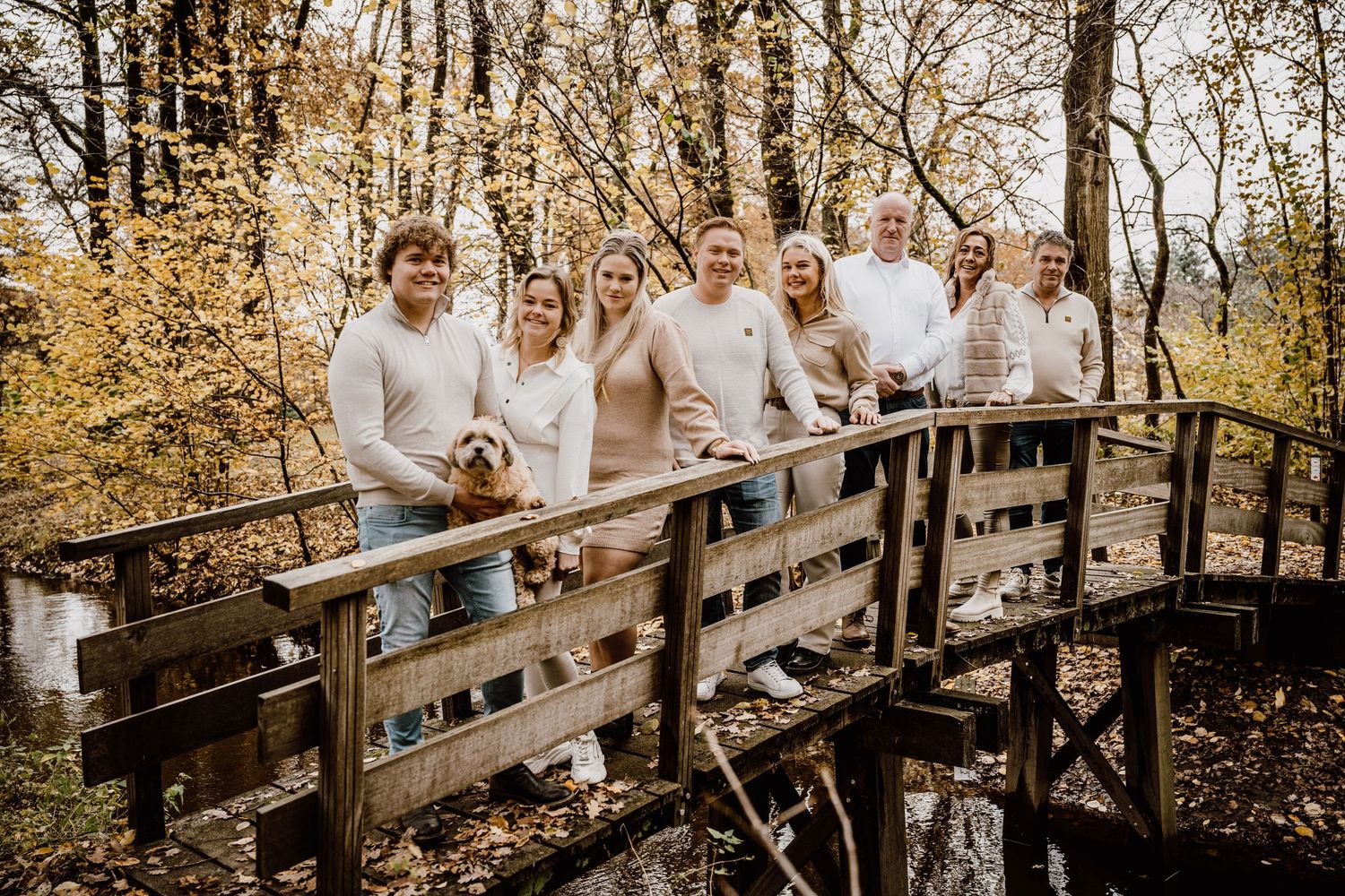 Group photo session on a wooden bridge surrounded by autumn trees with coordinated neutral outfits.