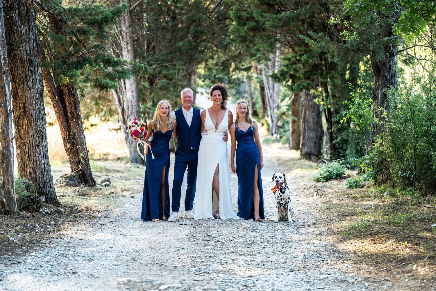 Wedding party walking along a tree-lined path during an outdoor celebration.