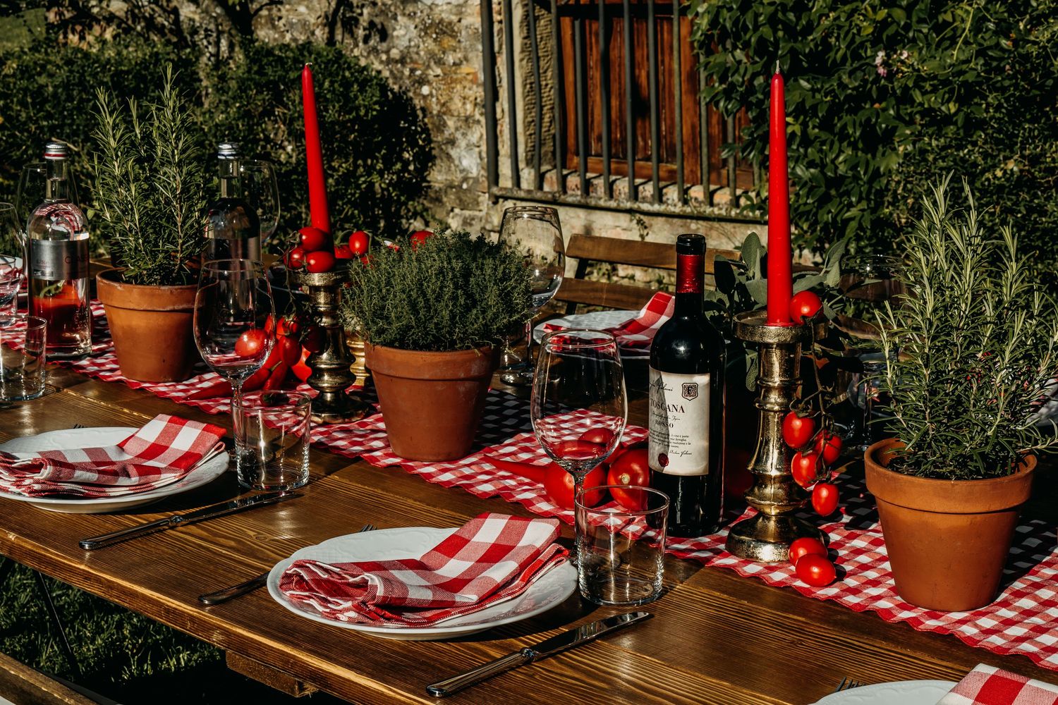 Elegant table setting with red and white checkered tablecloth, wine glasses, and rustic decor for outdoor dining.
