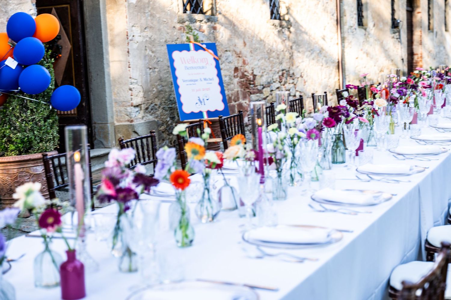 Elegant wedding reception table setting with colorful glass bottles and blue balloons.