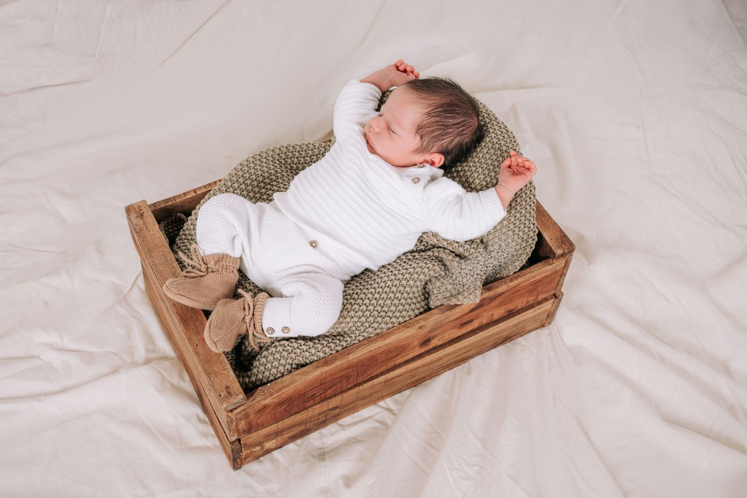 A series of photos showing a sleeping baby in a rustic wooden crate on white bedding.