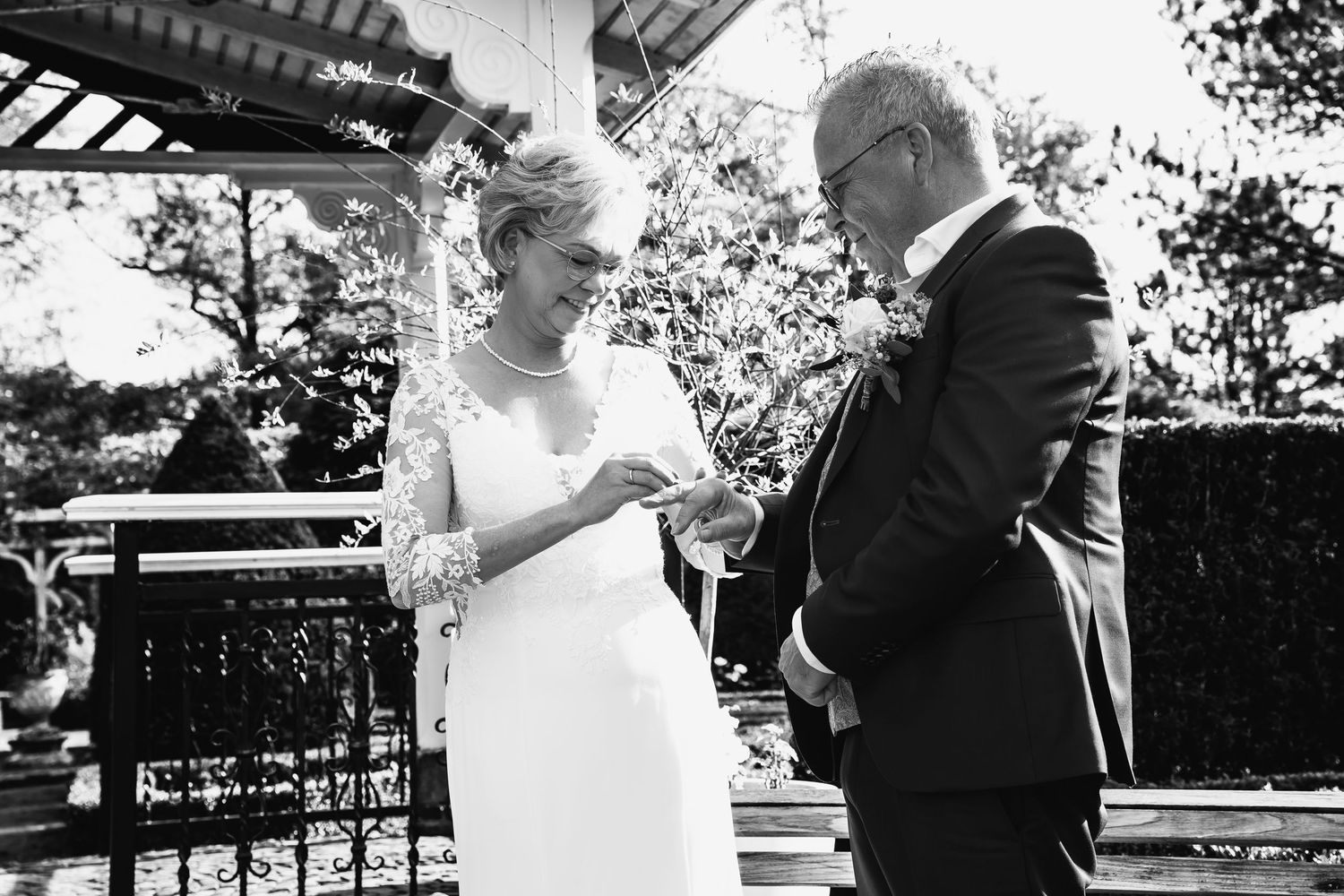 Wedding ceremony taking place under a wooden gazebo in a garden setting.