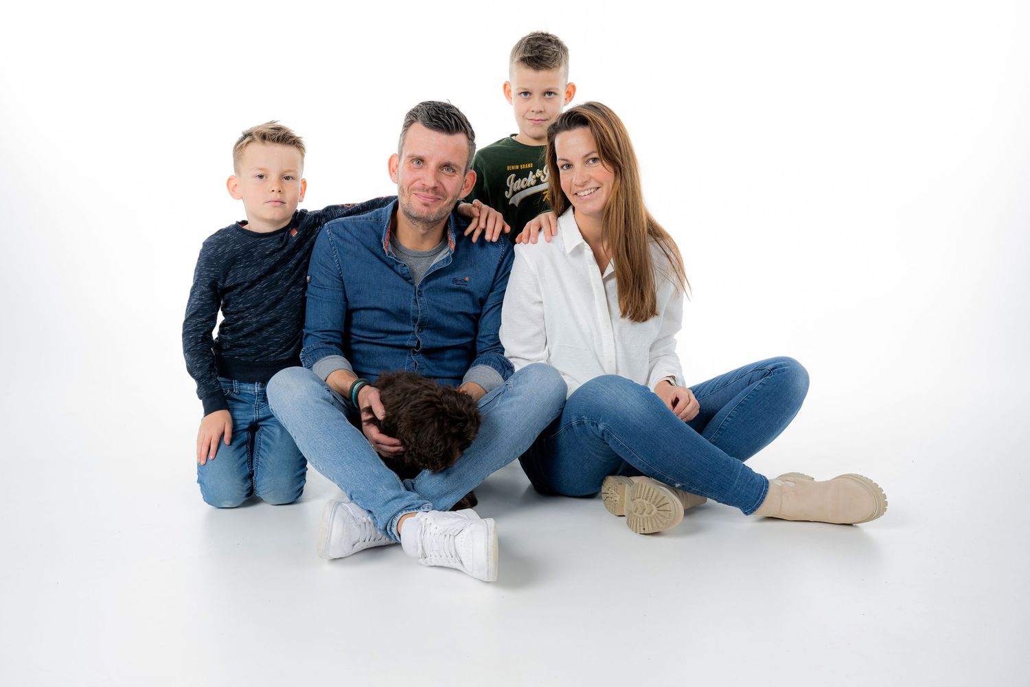 Family poses casually on white background in coordinated blue and neutral outfits.