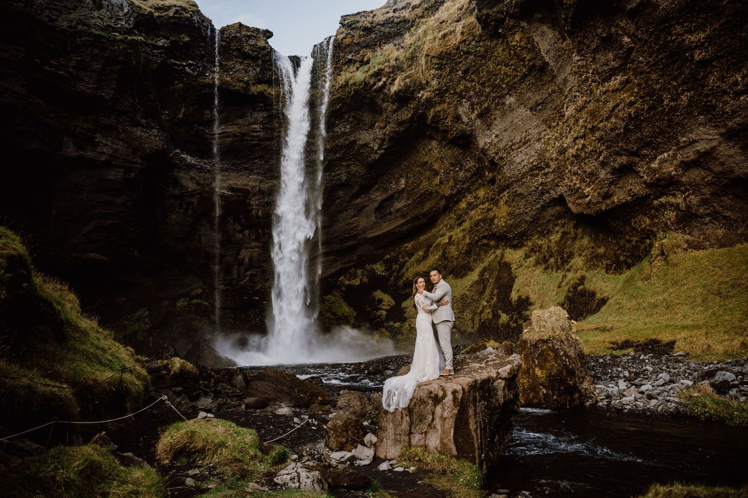 Scenic waterfall cascades down moss-covered cliffs in Iceland's rugged landscape during golden hour.