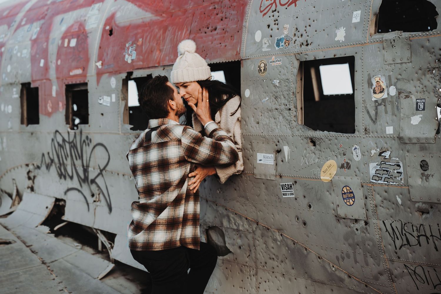 Person in plaid shirt taking photos against graffiti-covered concrete wall in urban setting.