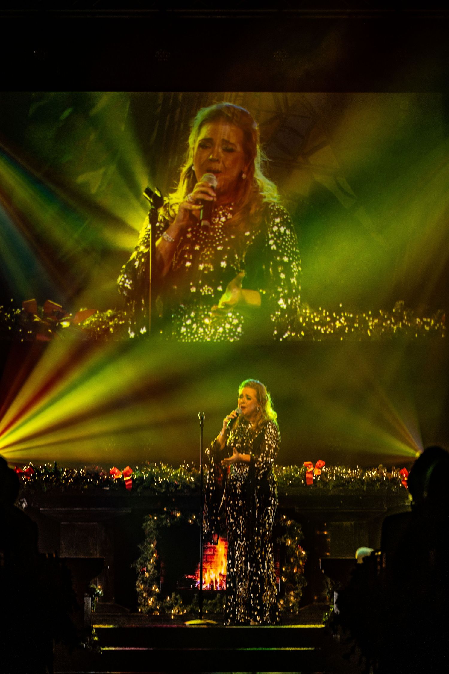 Stage performer in sparkly outfit surrounded by dramatic green and yellow lighting effects.