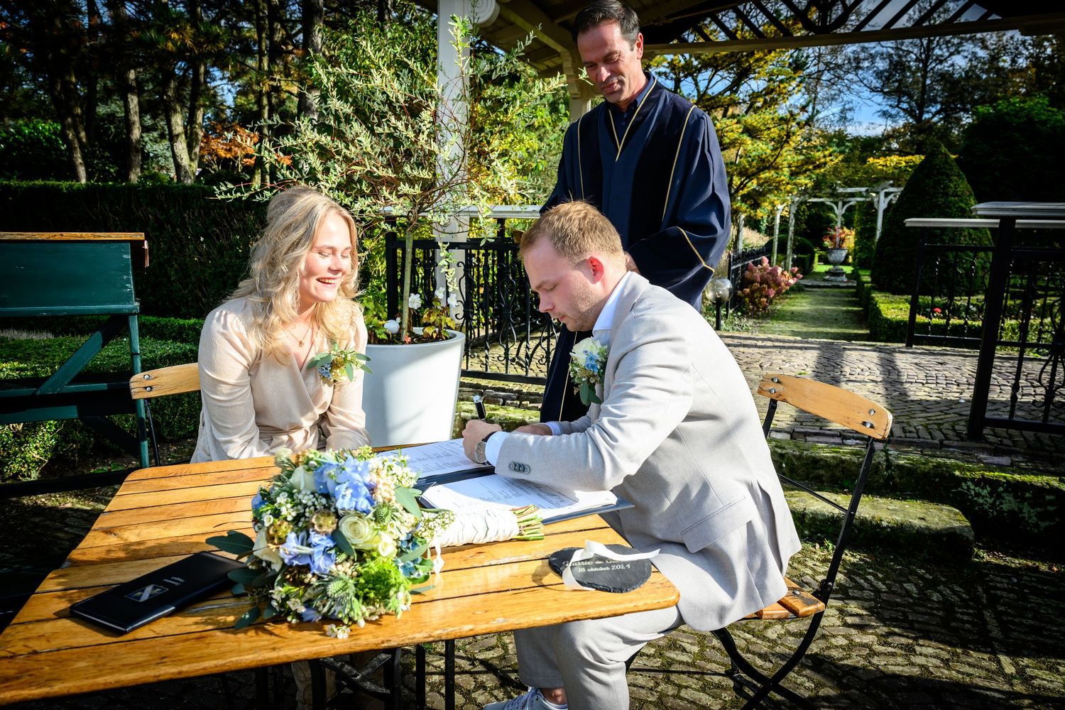 Wedding celebration at an outdoor wooden table decorated with blue flowers.